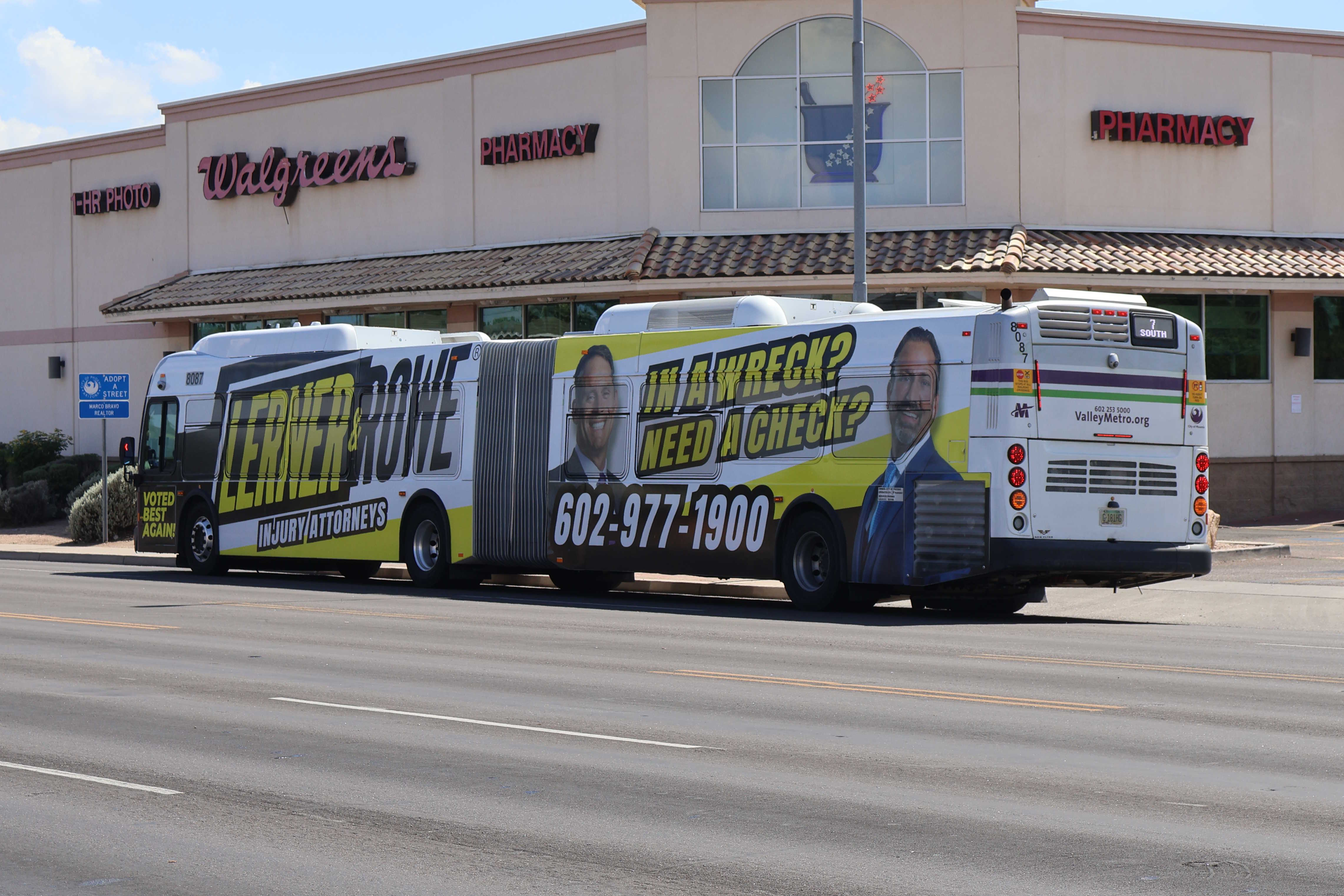 A white and gray articulated Valley Metro bus, with purple and green accent colors, number 8087, traveling southbound on 7th Street in Phoenix on route 7 to 7th Street and Dobbins Road