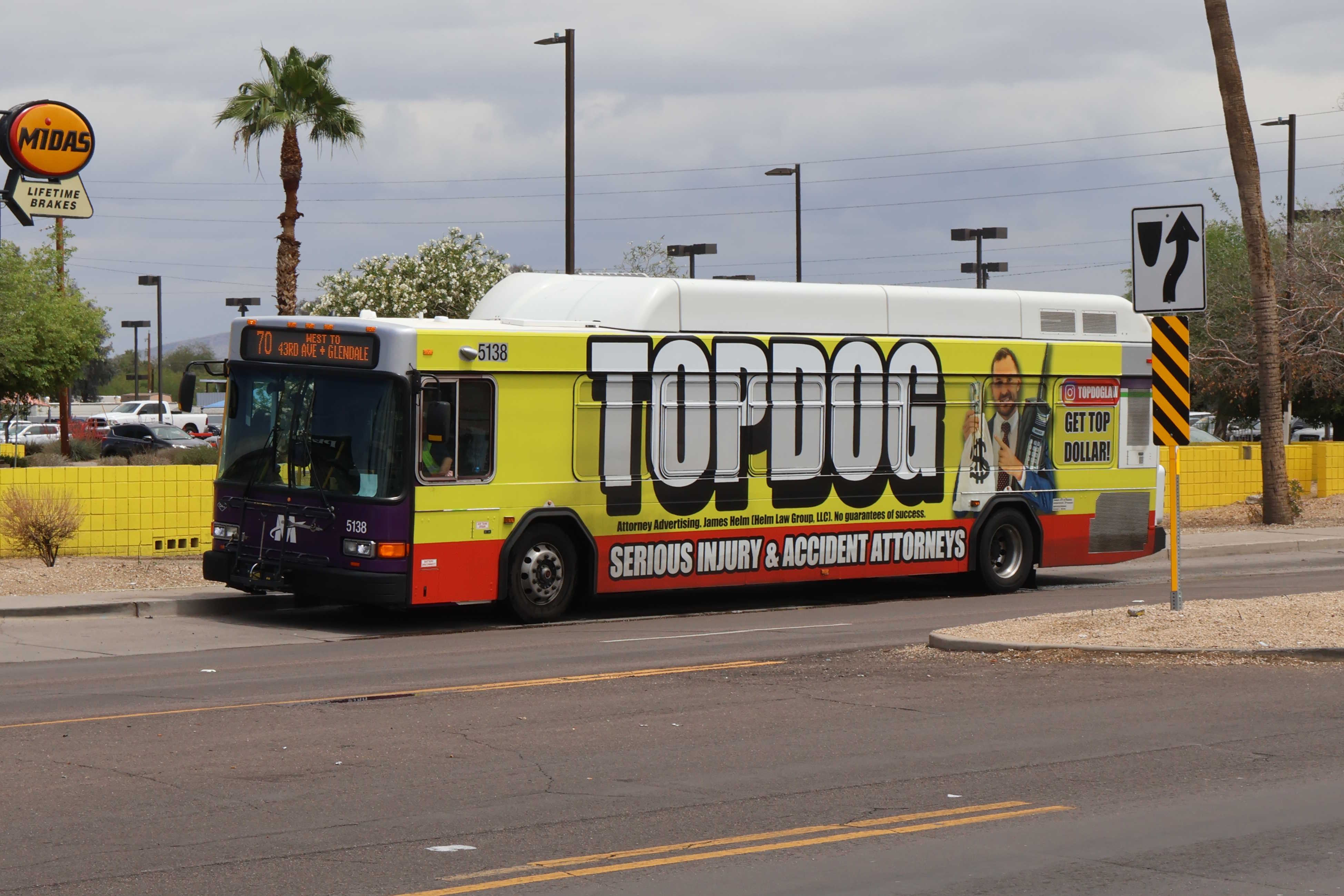 A white and gray Valley Metro bus, with purple and green accent colors, number 5138, traveling westbound on Glendale Avenue in Glendale on route 70 to Glendale Avenue and 43rd Avenue