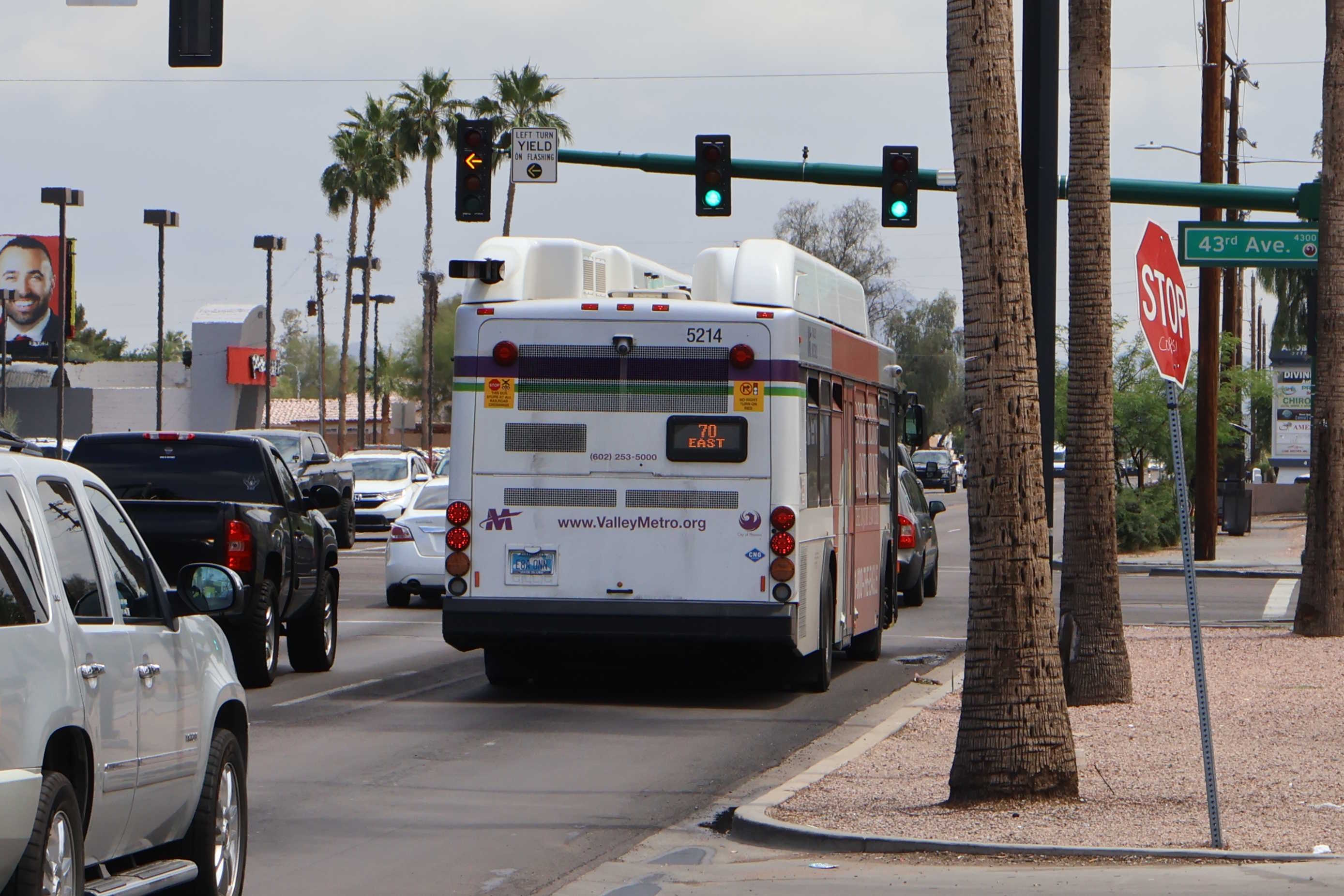 A white and gray Valley Metro bus, with purple and green accent colors, number 5214, traveling eastbound on Glendale Avenue in Glendale on route 70 to 24th Street / Baseline Park and Ride