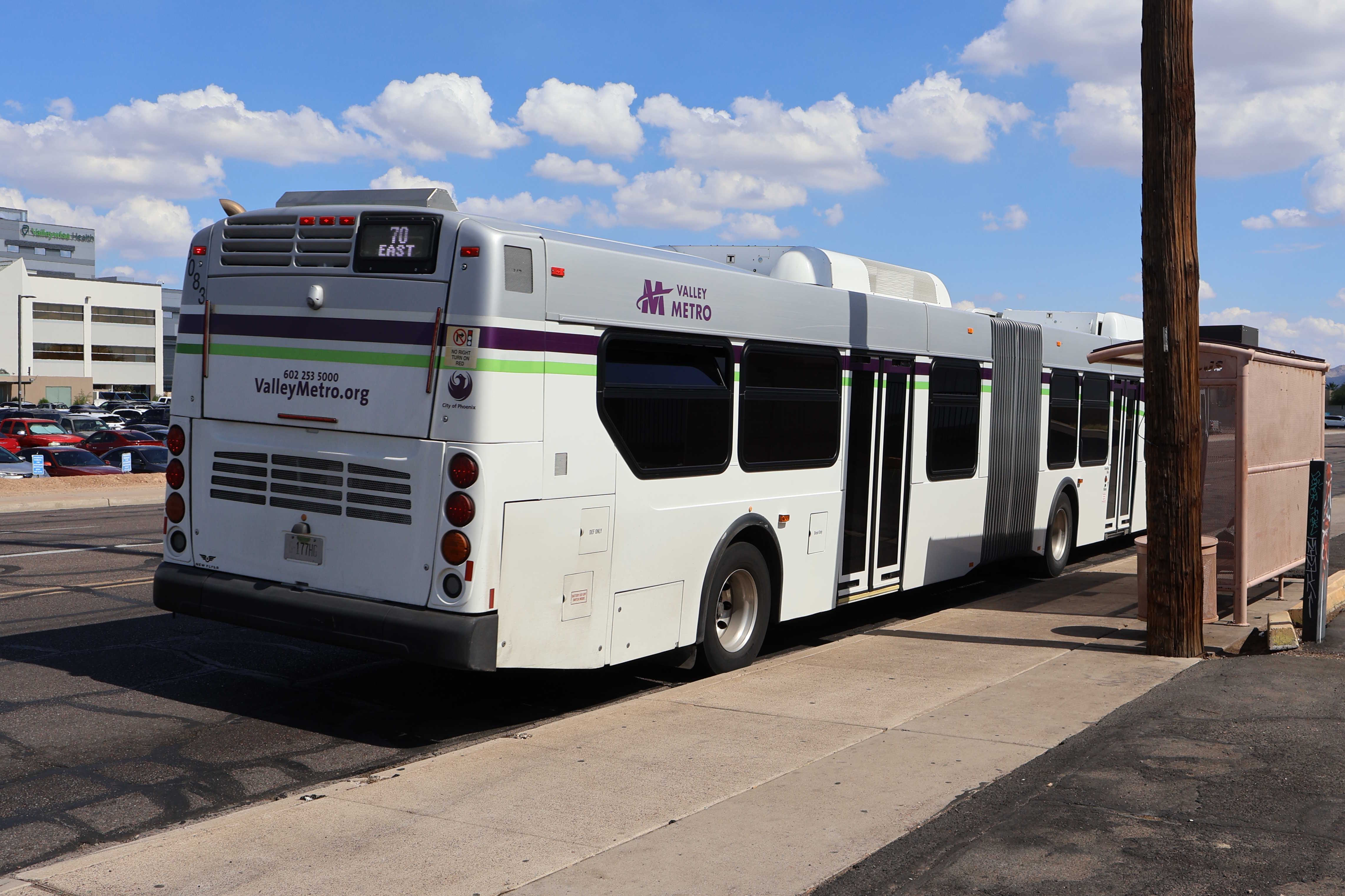 A white and gray articulated Valley Metro bus, with purple and green accent colors, number 8083, traveling southbound on 24th Street in Phoenix on route 70 to 24th Street / Baseline Park and Ride