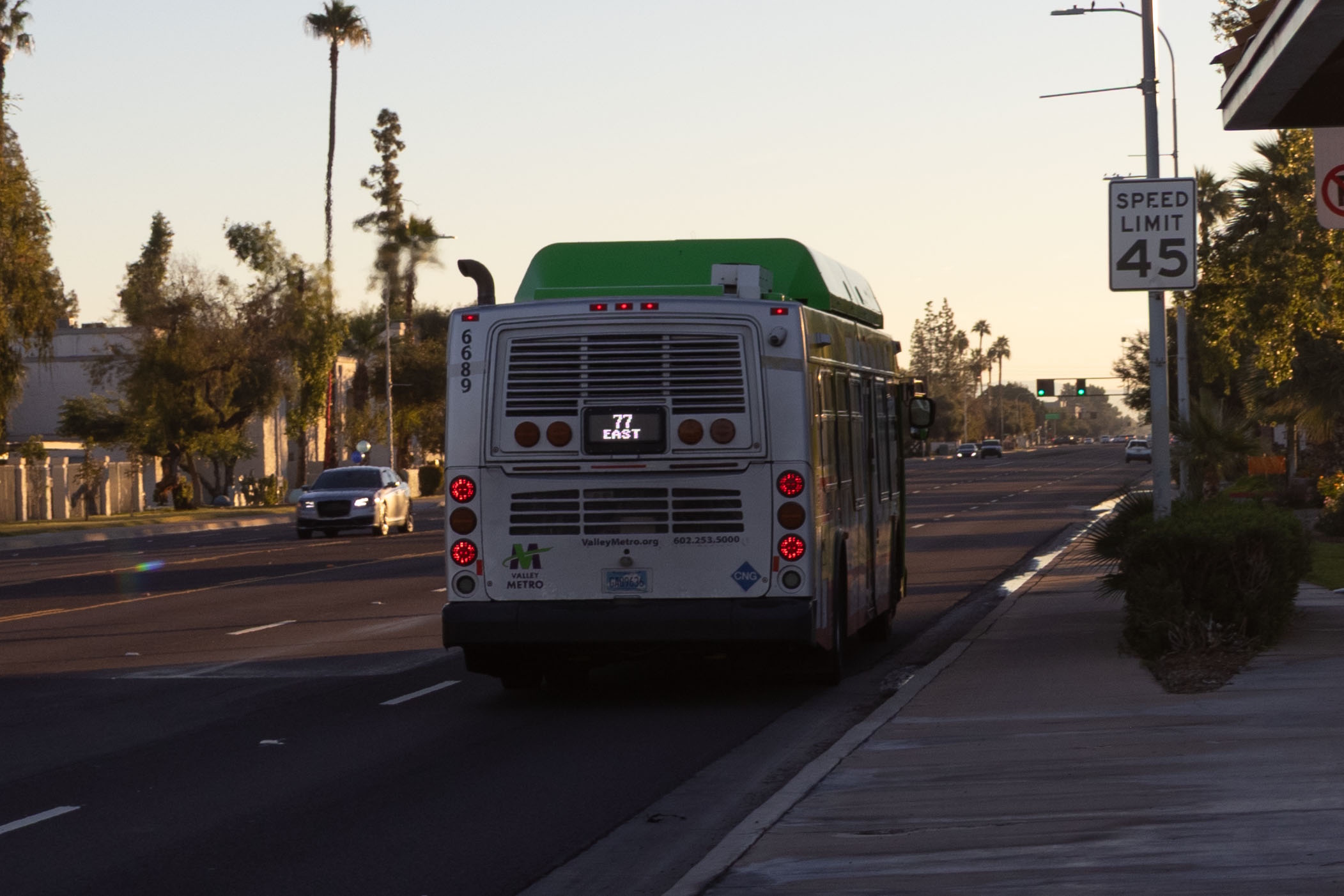 A gray and green Valley Metro bus, number 6689, traveling eastbound on Baseline Road in Tempe on route 77 to West Mesa Park and Ride