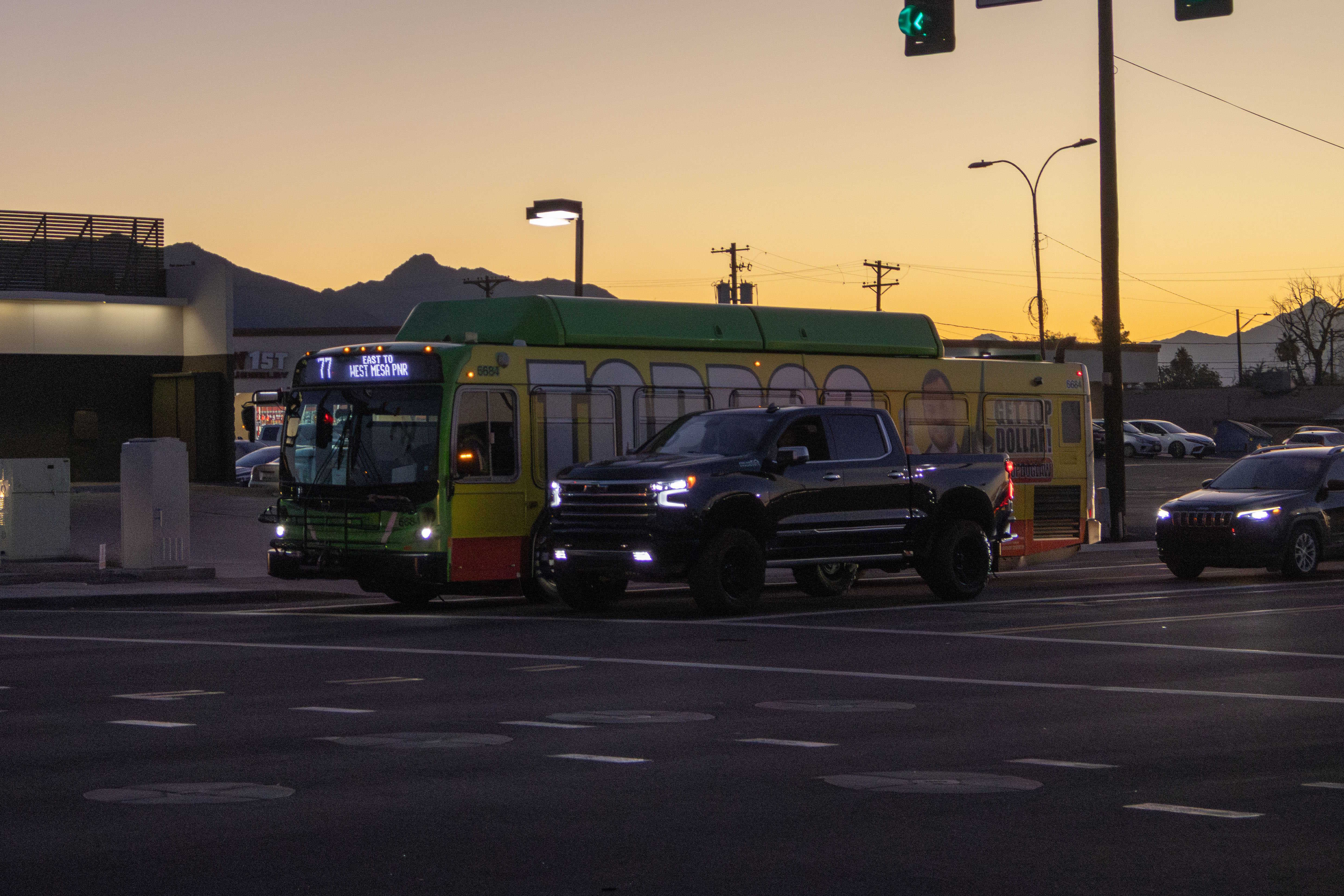 A gray and green Valley Metro bus, number 6684, traveling eastbound on Baseline Road in Phoenix on route 77 to West Mesa Park and Ride