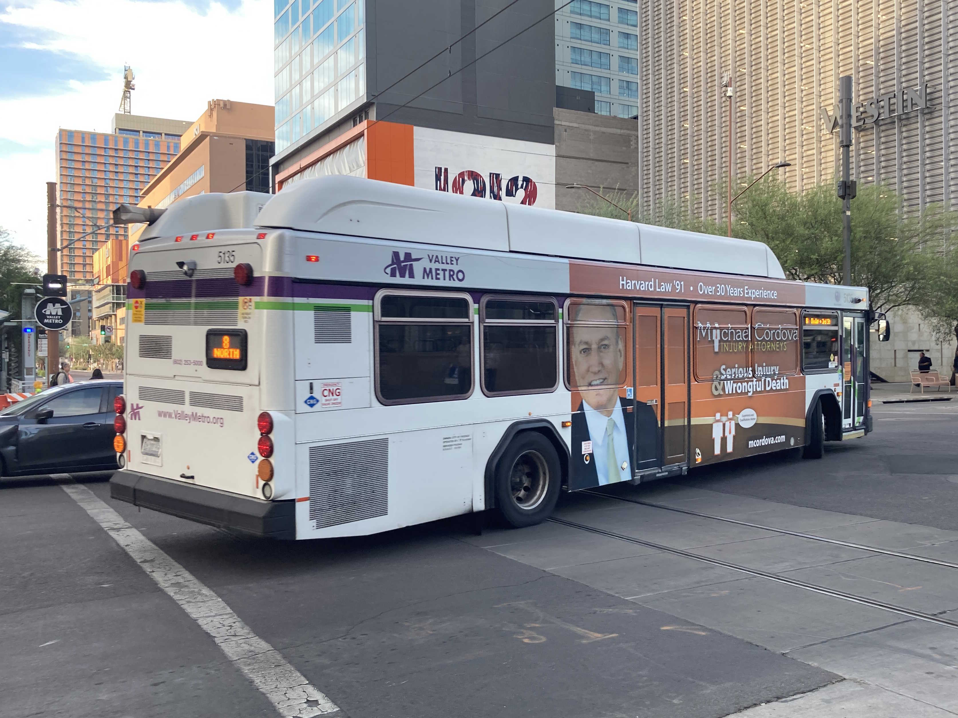 A white and gray Valley Metro bus, with purple and green accent colors, number 5135, traveling eastbound on Van Buren Street in Phoenix on route 8 to Dunlap Avenue and 3rd Street