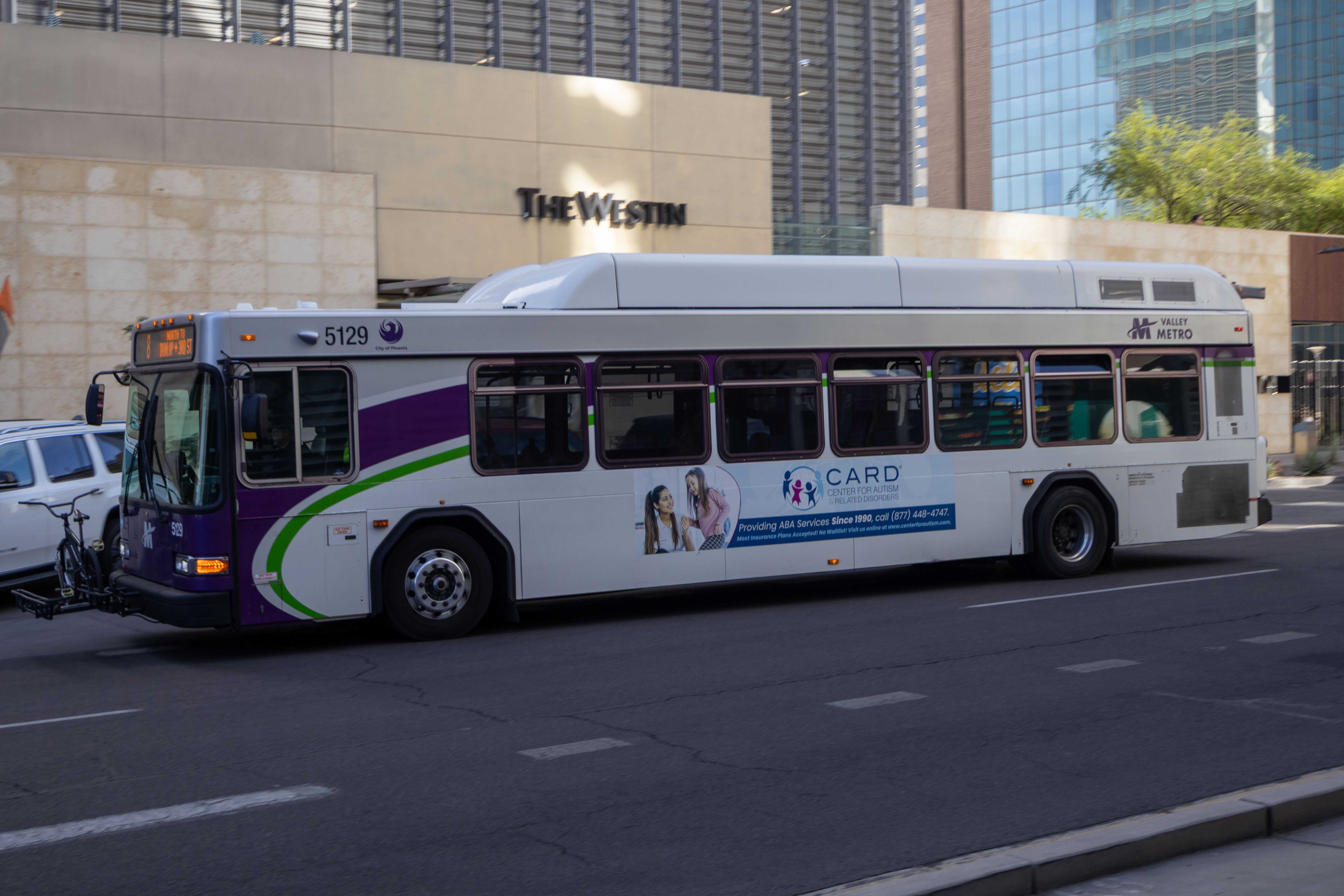 A white and gray Valley Metro bus, with purple and green accent colors, number 5129, traveling northbound on Central Avenue in Phoenix on route 8 to Dunlap Avenue and 3rd Street