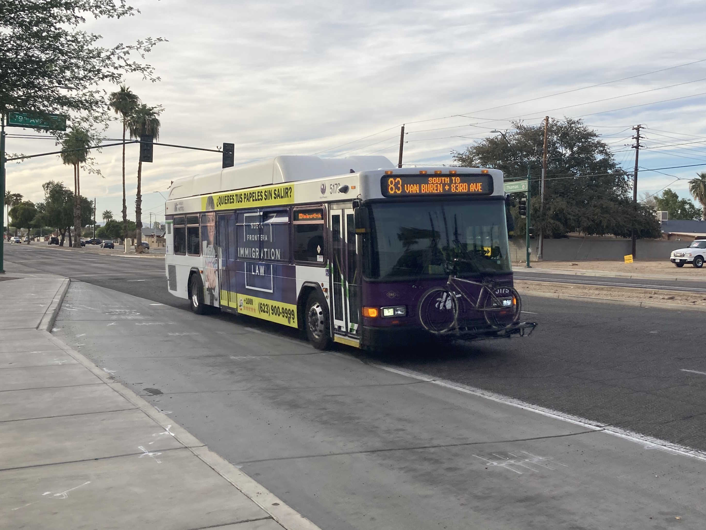 A white and gray Valley Metro bus, with purple and green accent colors, number 5179, traveling eastbound on Thomas Road in Phoenix on route 83 to 83rd Avenue and Van Buren Street