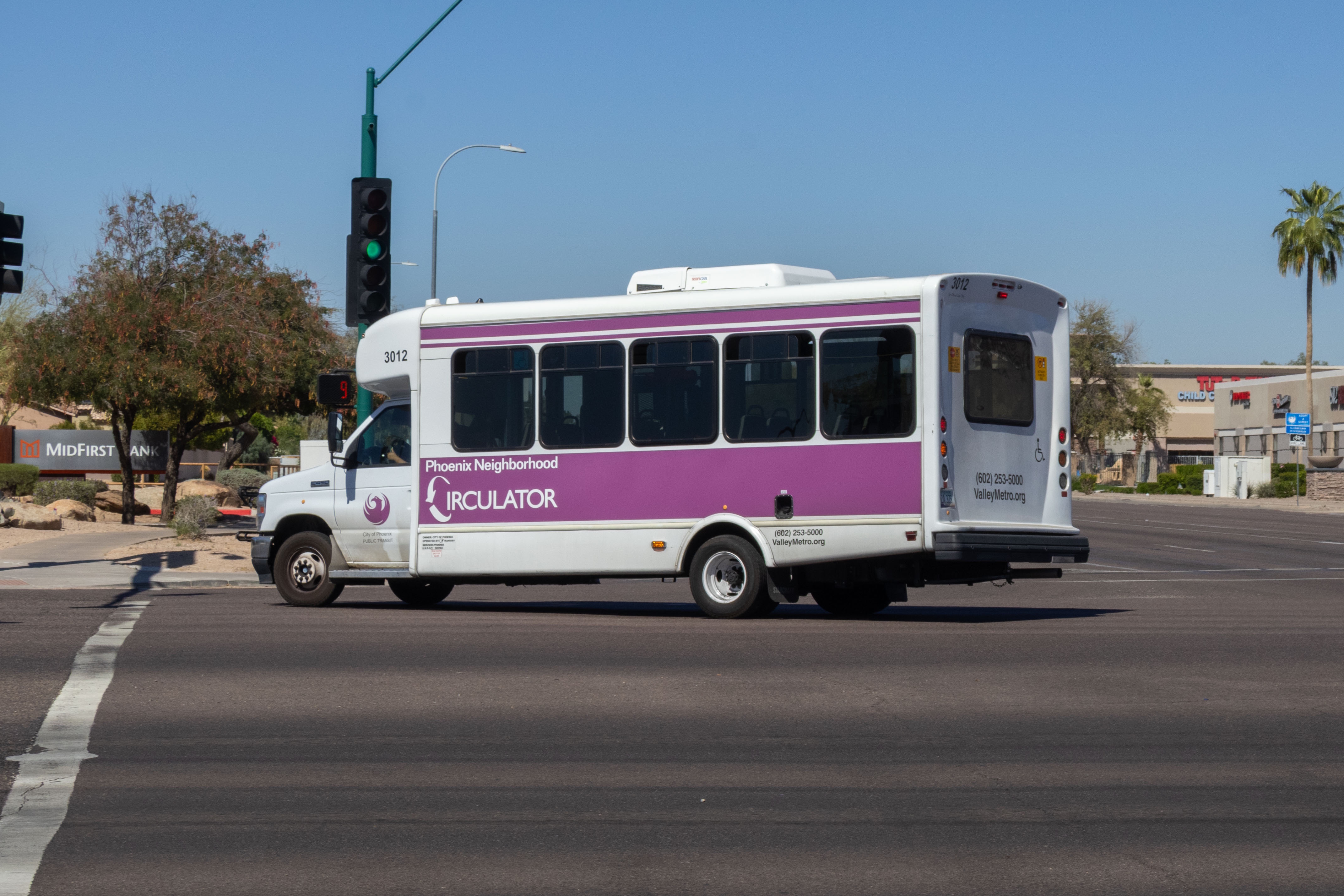 A white and purple Phoenix Neighborhood Circulator minibus, number 3012, traveling westbound on Chandler Boulevard in Phoenix on the ALEX route to Desert Foothills