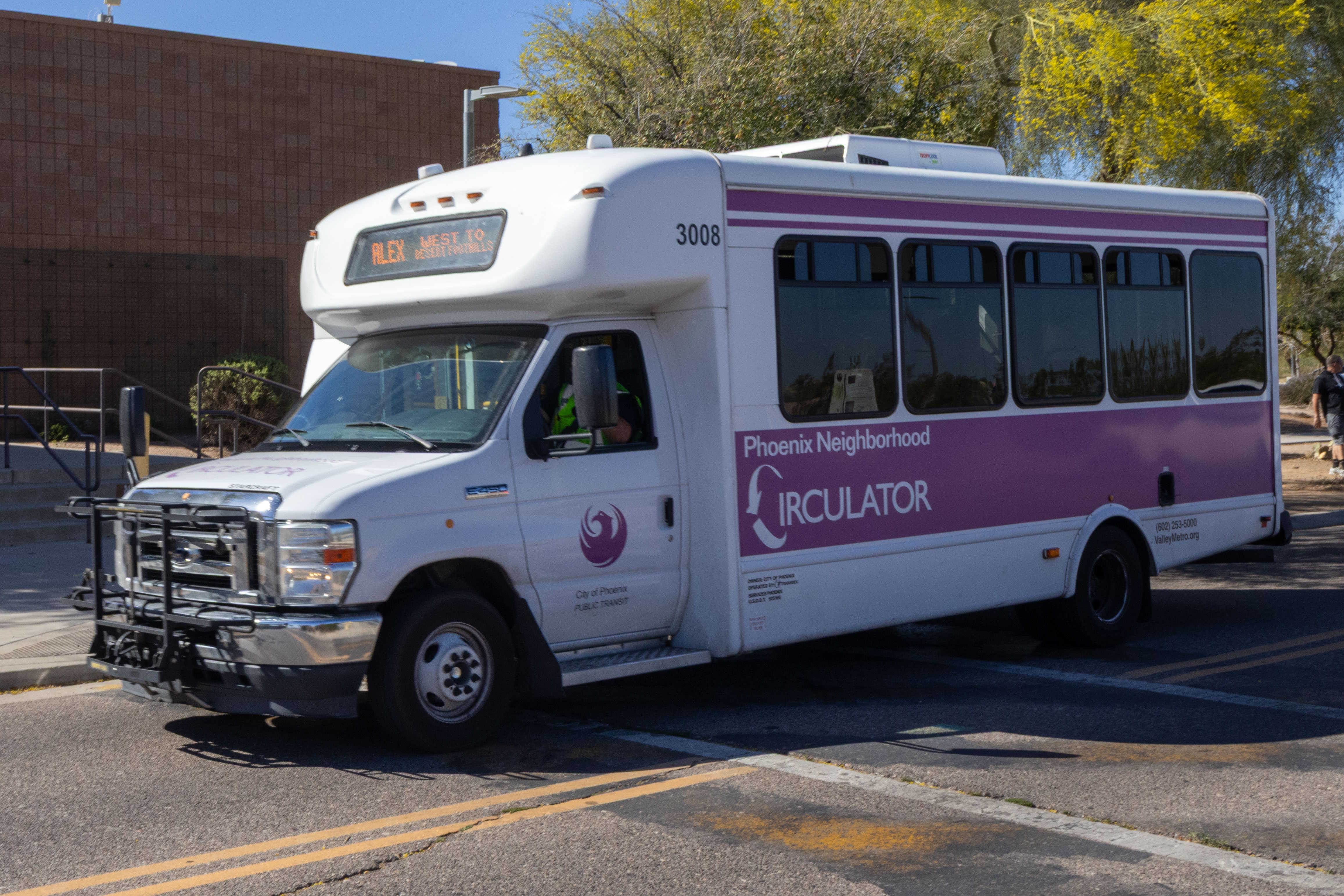 A white and purple Phoenix Neighborhood Circulator minibus, number 3008, traveling southbound on 48th Street in Phoenix on the ALEX route to Desert Foothills