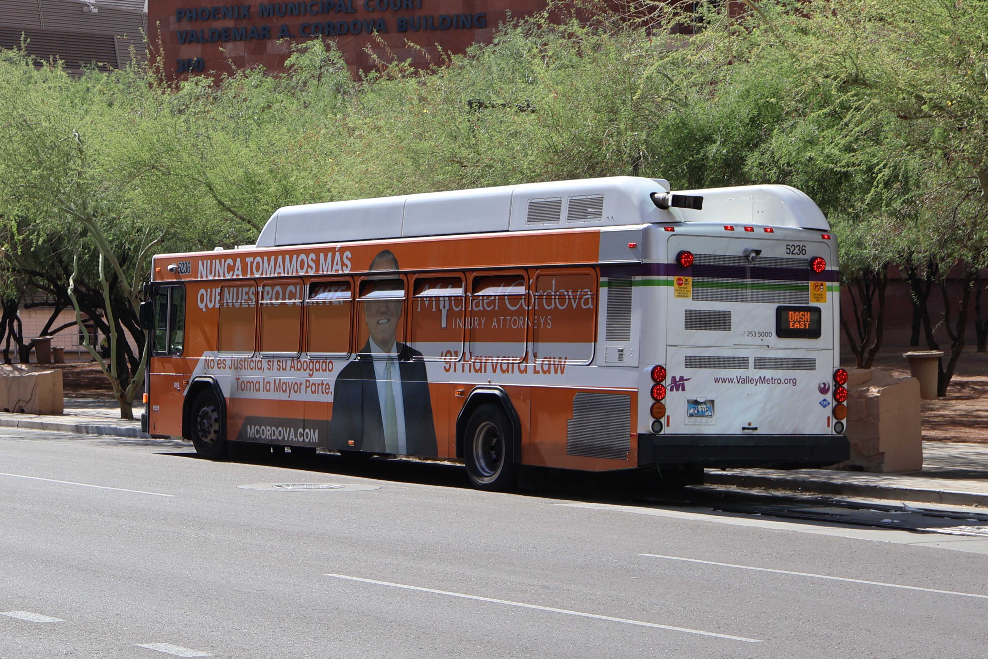 A white and gray Valley Metro bus, with purple and green accent colors, number 5236, traveling westbound on Washington Street in Phoenix on the DASH route to Washington Street and 4th Avenue