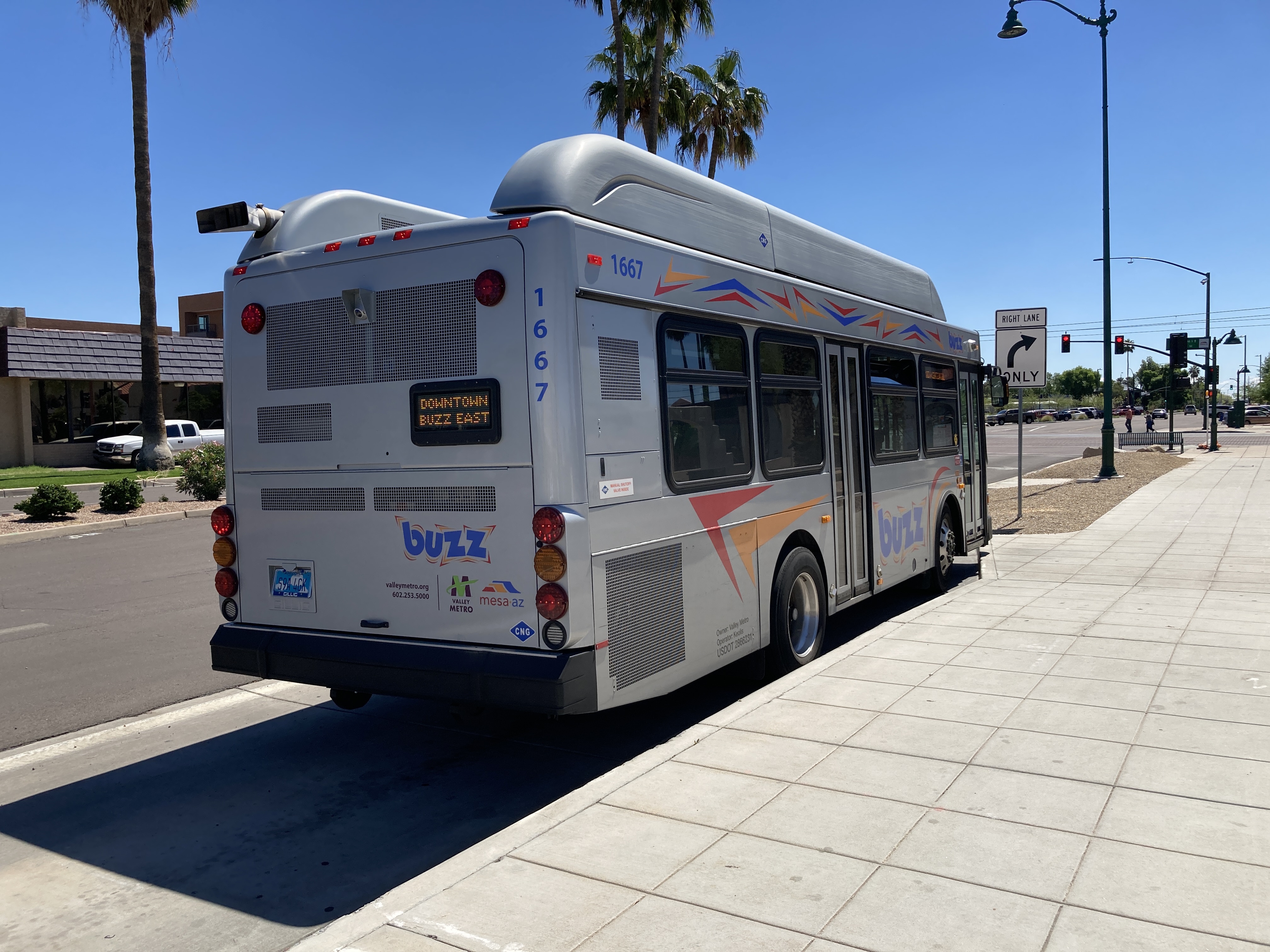 A silver BUZZ bus, with red, orange, and blue accents, number 1667, at Centennial Way and Main Street in Mesa on the Downtown BUZZ route to Centennial Way and Main Street