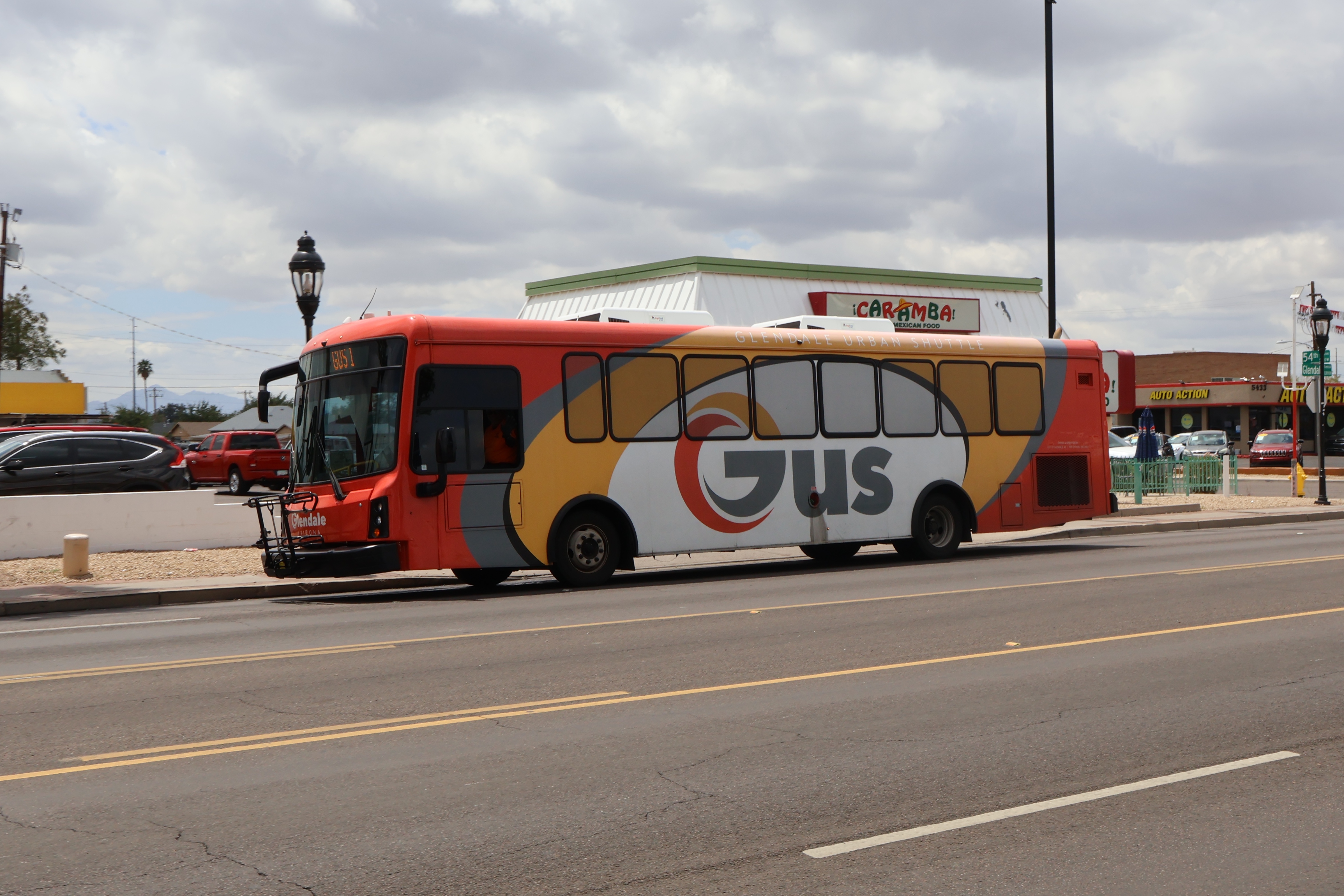 An orange, yellow, and white GUS bus, number 6354D12, traveling eastbound on Glendale Avenue in Glendale on GUS 1 to Glendale City Hall