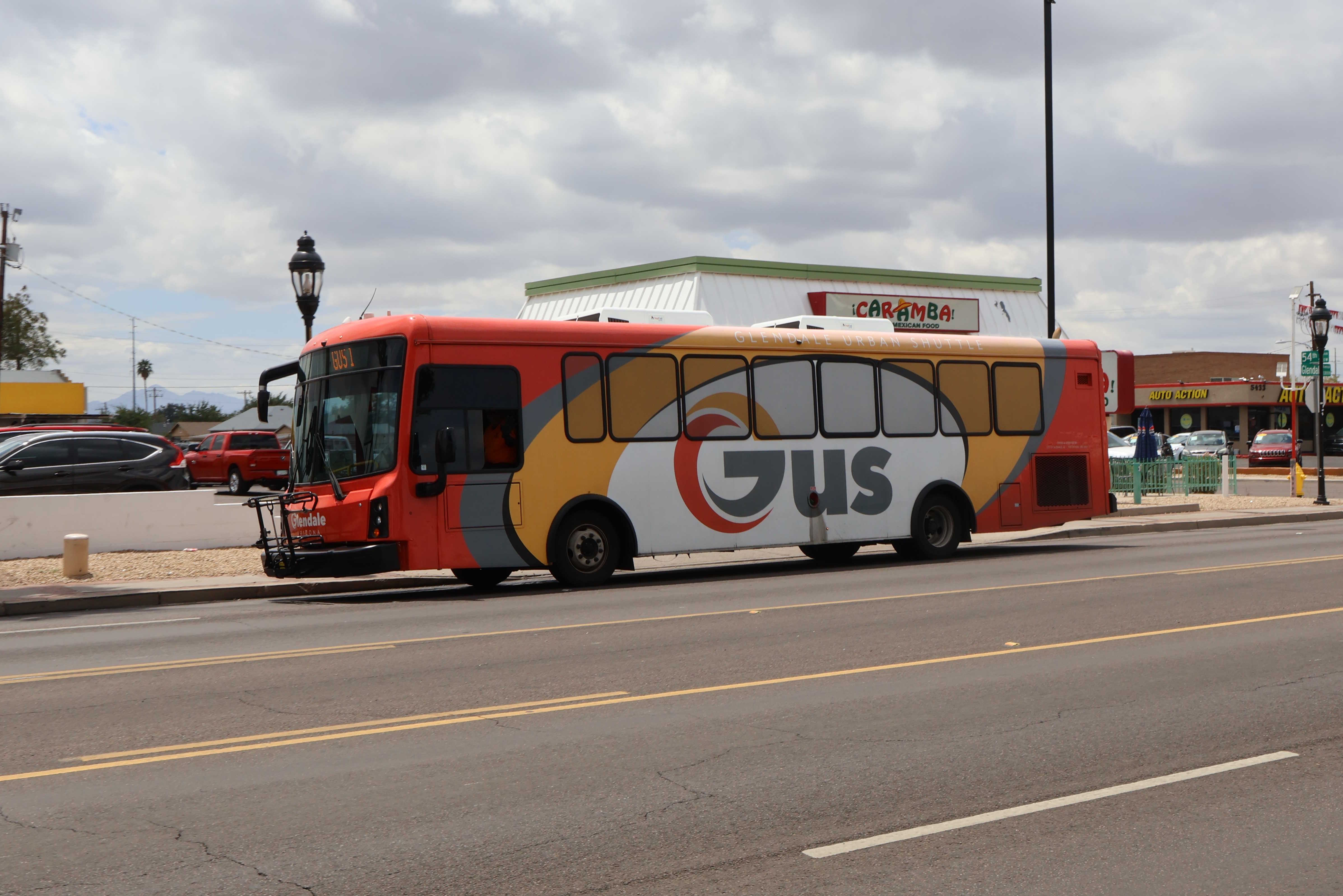 An orange, yellow, and white GUS bus, number 6354D12, traveling eastbound on Glendale Avenue in Glendale on GUS 1 to Glendale City Hall