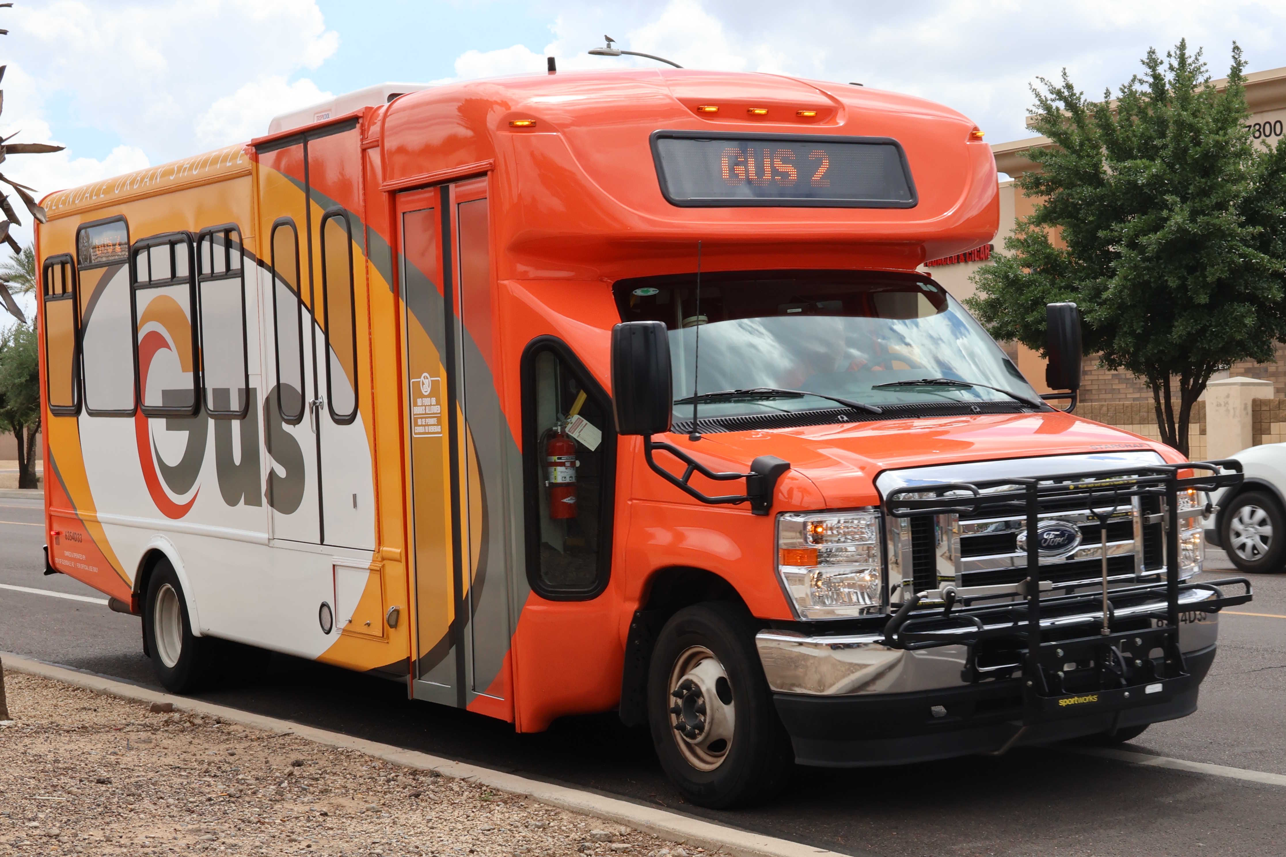 An orange, yellow, and white GUS minibus, number 6354D33, traveling northbound on 55th Avenue in Glendale on GUS 2 to Tanner Terrace