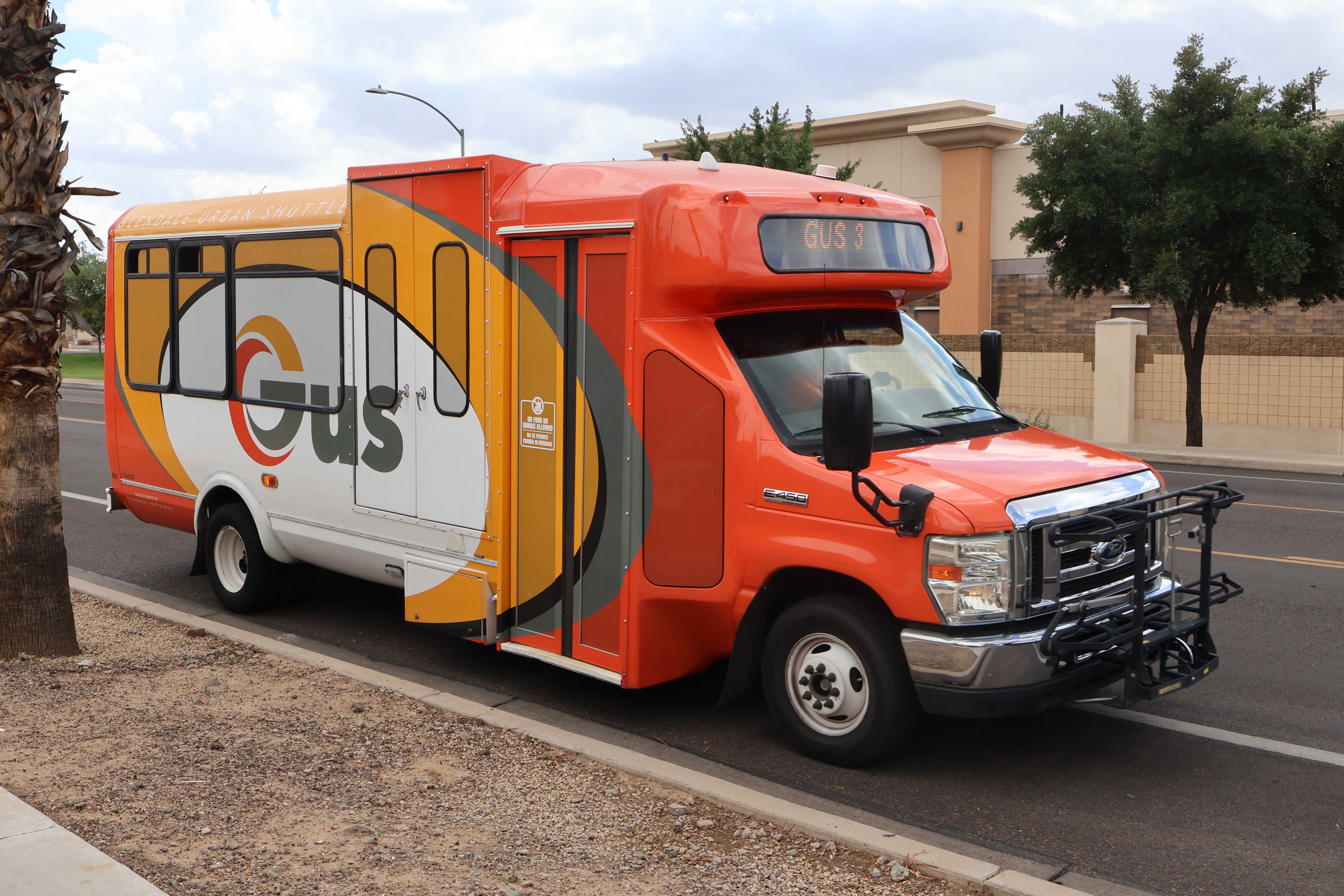 An orange, yellow, and white GUS minibus, number 6354D29, traveling northbound on 55th Avenue in Glendale on GUS 3 to Manistee Manor