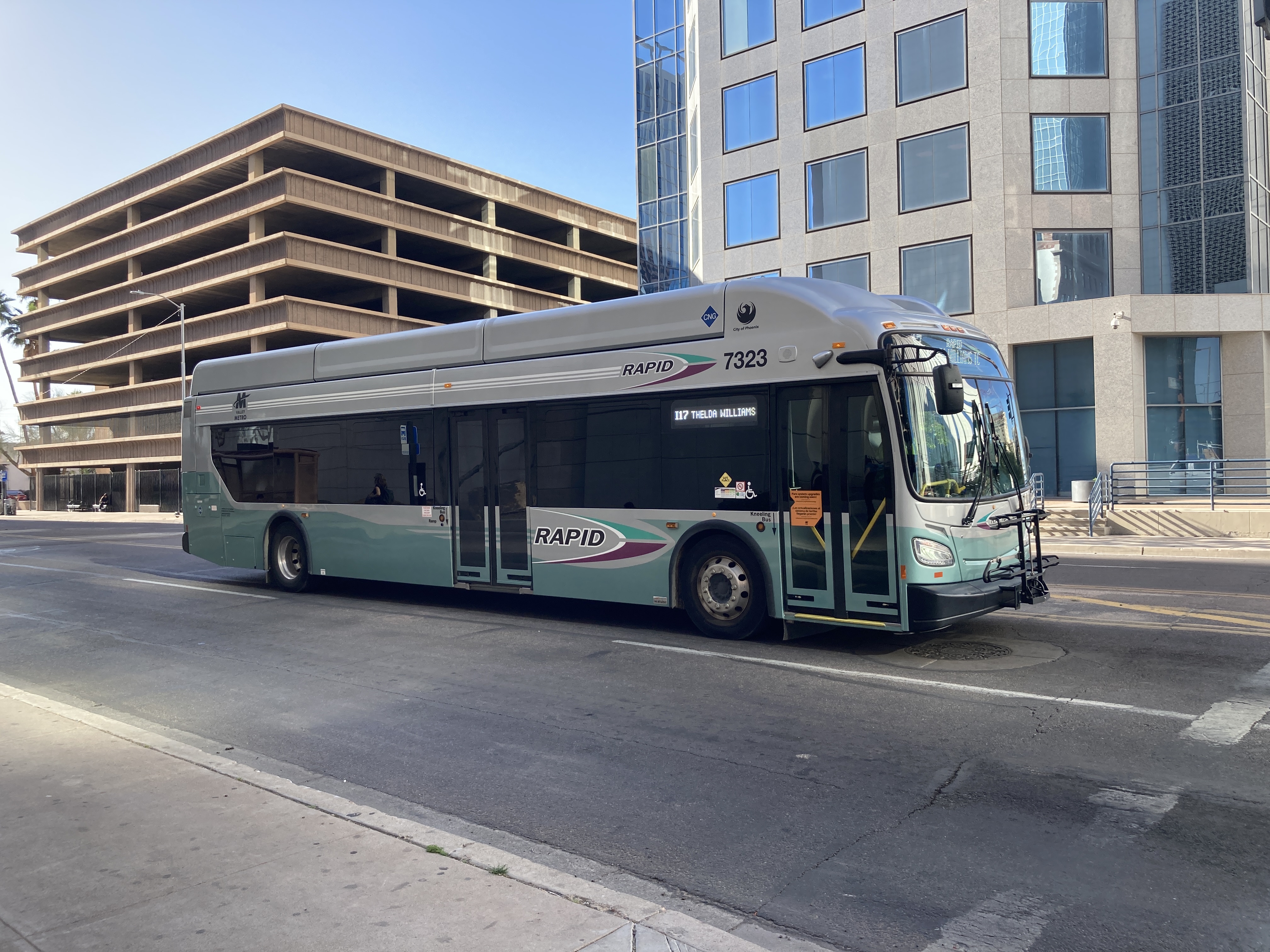 A silver and bluish-green Valley Metro RAPID bus, number 7323, traveling eastbound on Van Buren Street in Phoenix on the I-17 RAPID route to Happy Valley Park and Ride