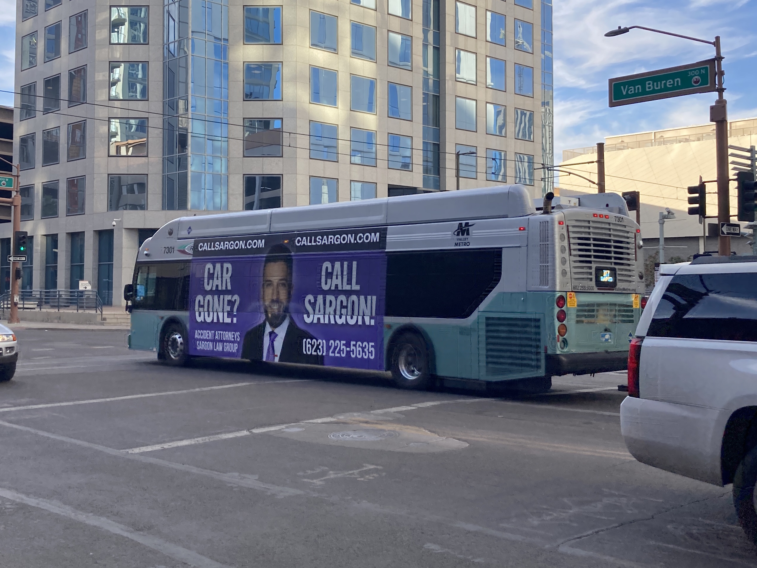 A silver and bluish-green Valley Metro RAPID bus, number 7301, traveling westbound on Van Buren Street in Phoenix on the I-17 RAPID route to Happy Valley Park and Ride