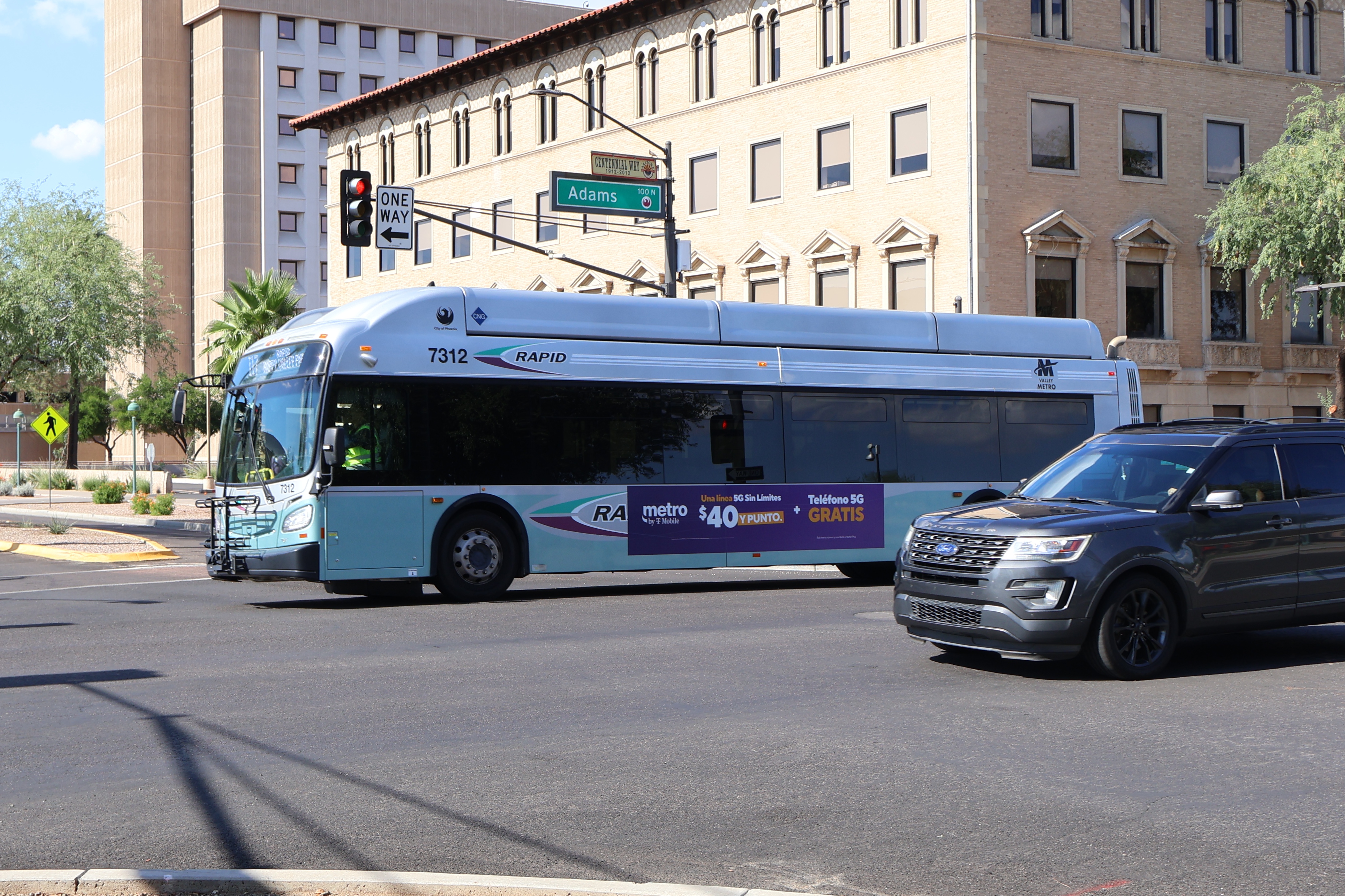 A silver and bluish-green Valley Metro RAPID bus, number 7312, traveling westbound on Adams Street in Phoenix on the I-17 RAPID route to Happy Valley Park and Ride
