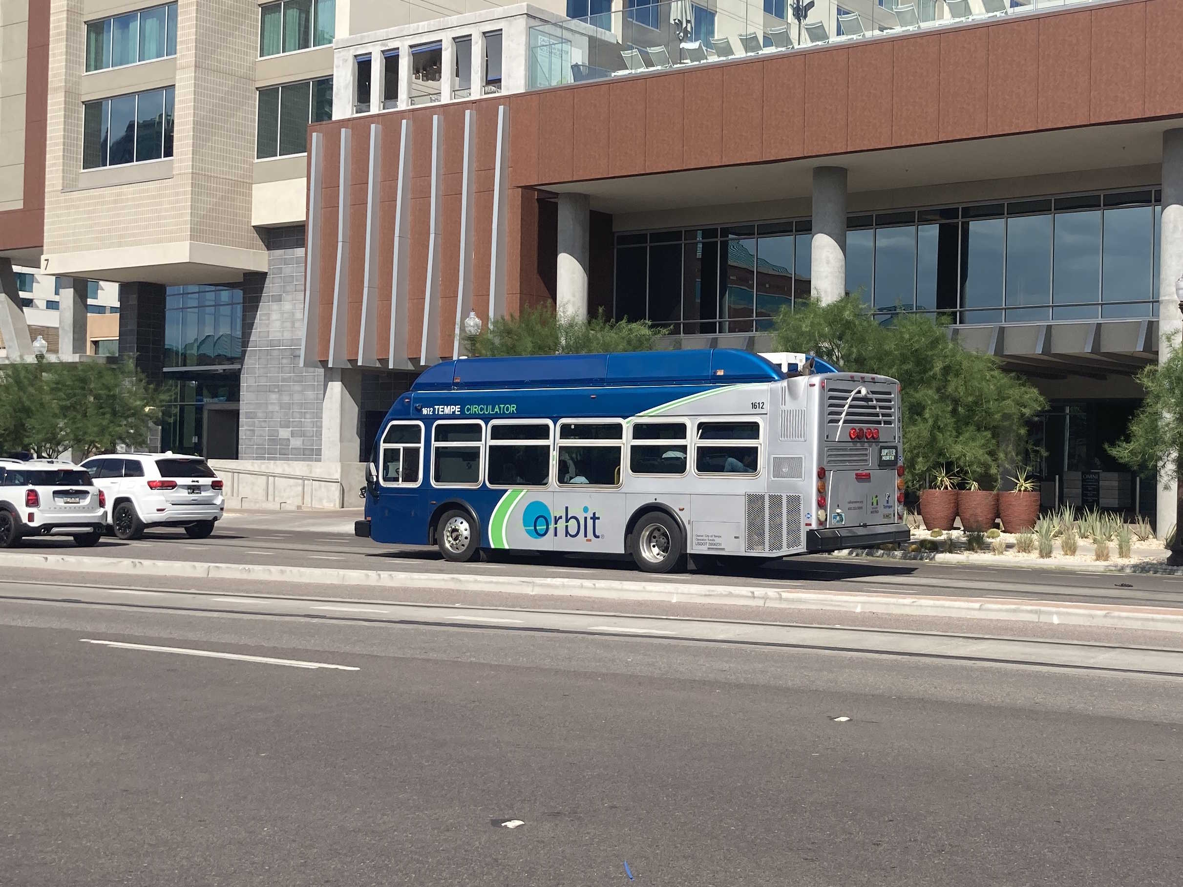 A gray and blue Orbit bus, with a green stripe, number 1612, traveling northbound on Mill Avenue on the Jupiter route to Tempe Transportation Center