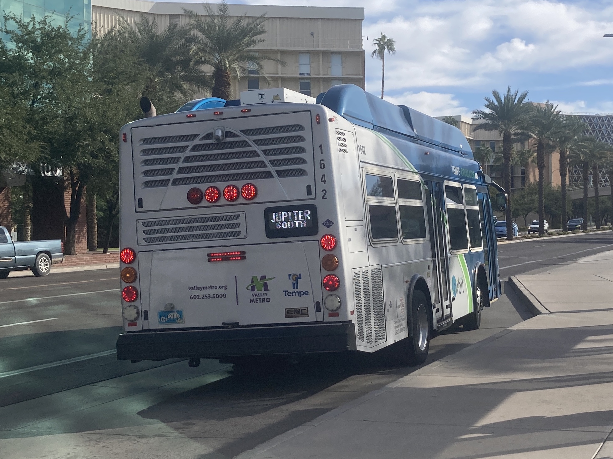 A gray and blue Orbit bus, with a green stripe, number 1642, traveling eastbound on University Drive on the Jupiter route to McClintock High School