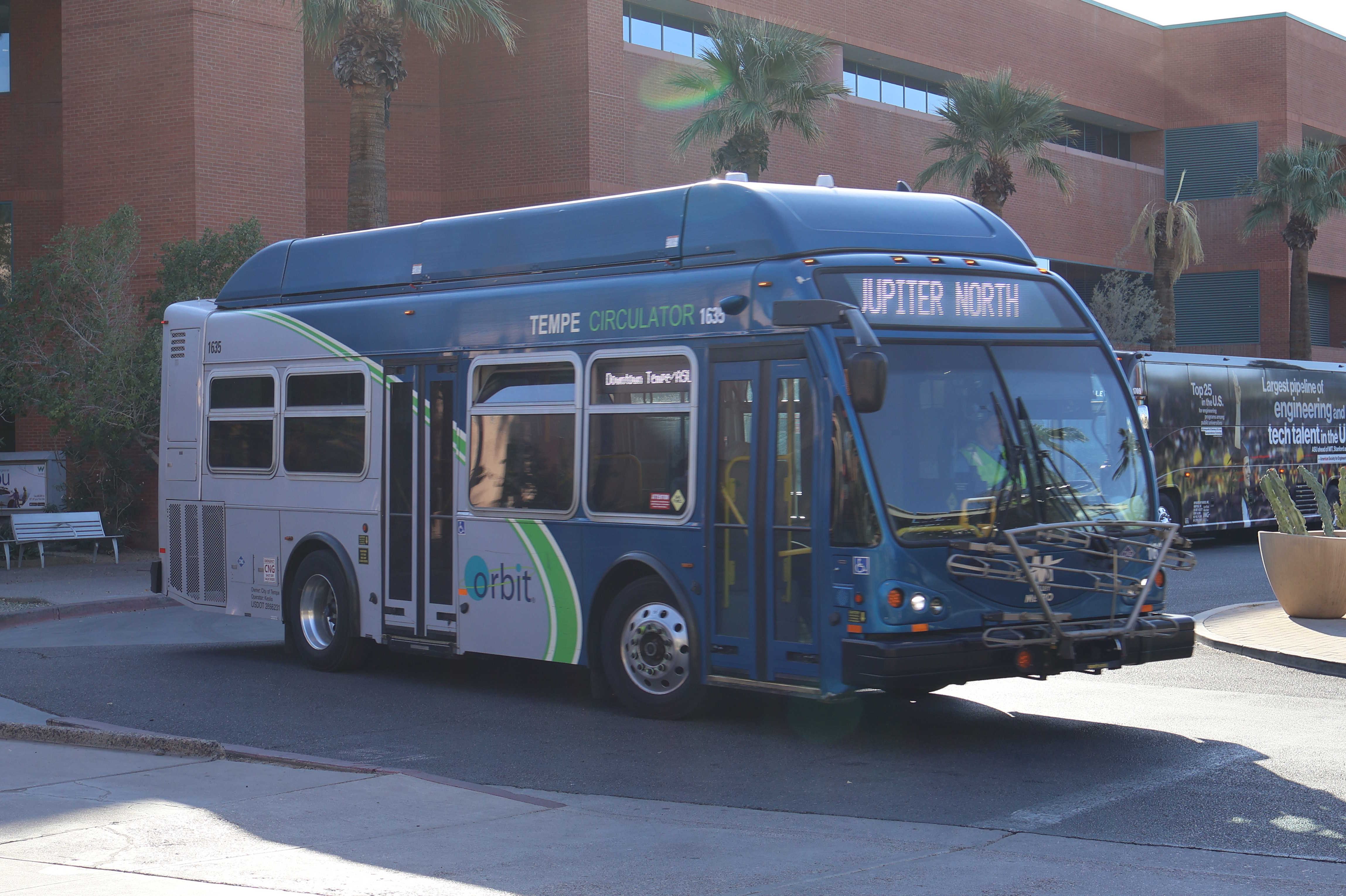 A gray and blue Orbit bus, with a green stripe, number 1635, traveling westbound on Gammage Parkway on the Jupiter route to Tempe Transportation Center