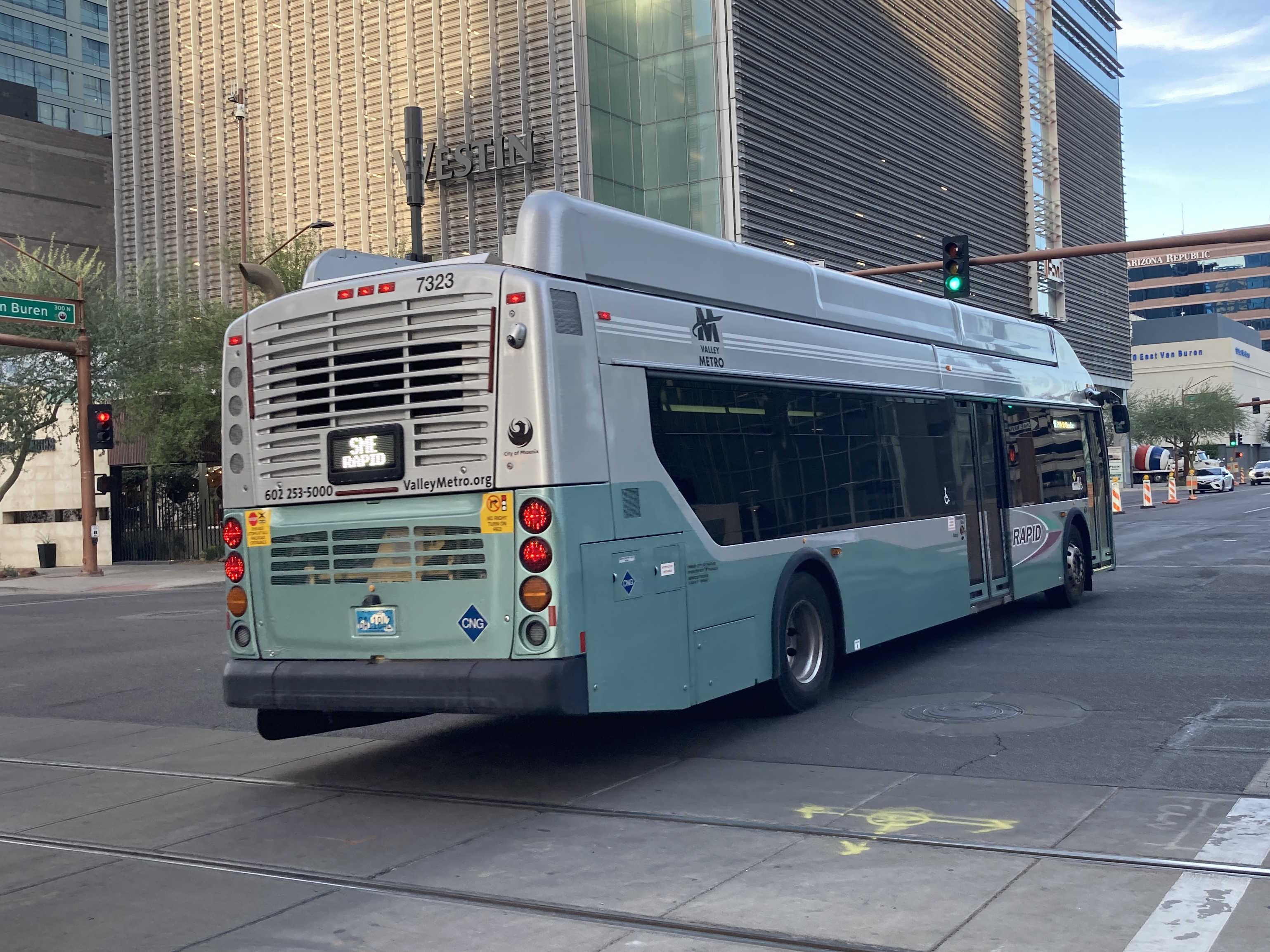 A silver and bluish-green Valley Metro RAPID bus, number 7323, traveling eastbound on Van Buren Street in Phoenix on the South Mountain East RAPID route to 24th Street and Baseline Park and Ride