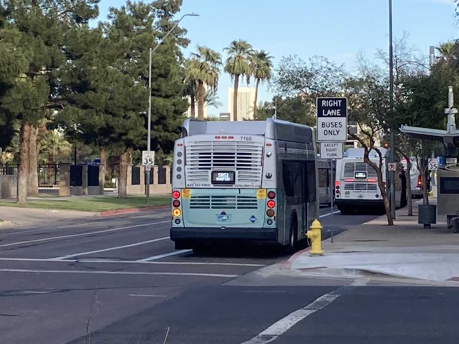 A silver and bluish-green Valley Metro RAPID bus, number 7165, traveling eastbound on Jefferson Street in Phoenix on the State Route 51 RAPID route to Bell Road and State Route 51 Park and Ride