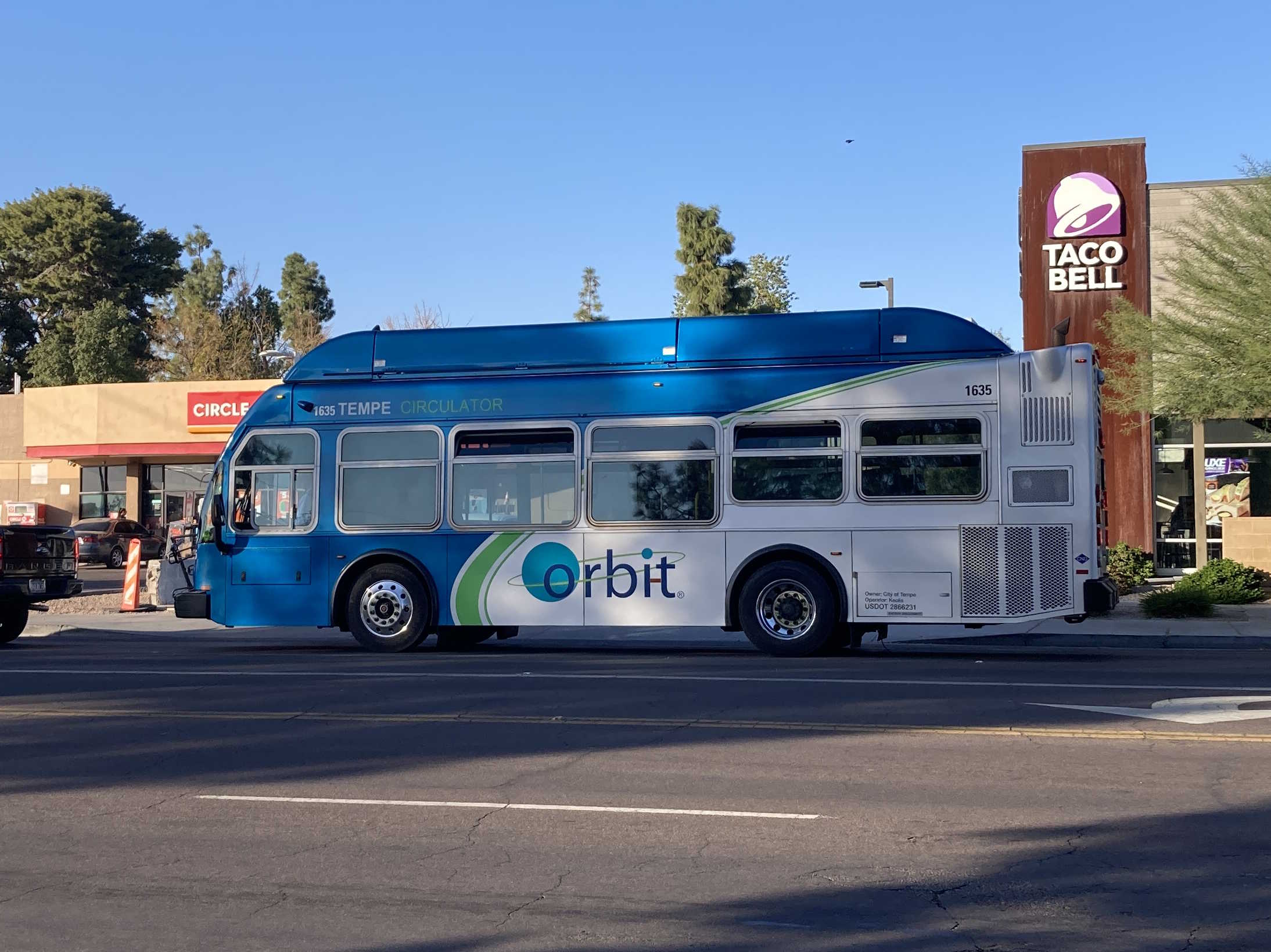 A gray and blue Orbit bus, with a green stripe, number 1635, traveling westbound on University Drive on Venus Forward