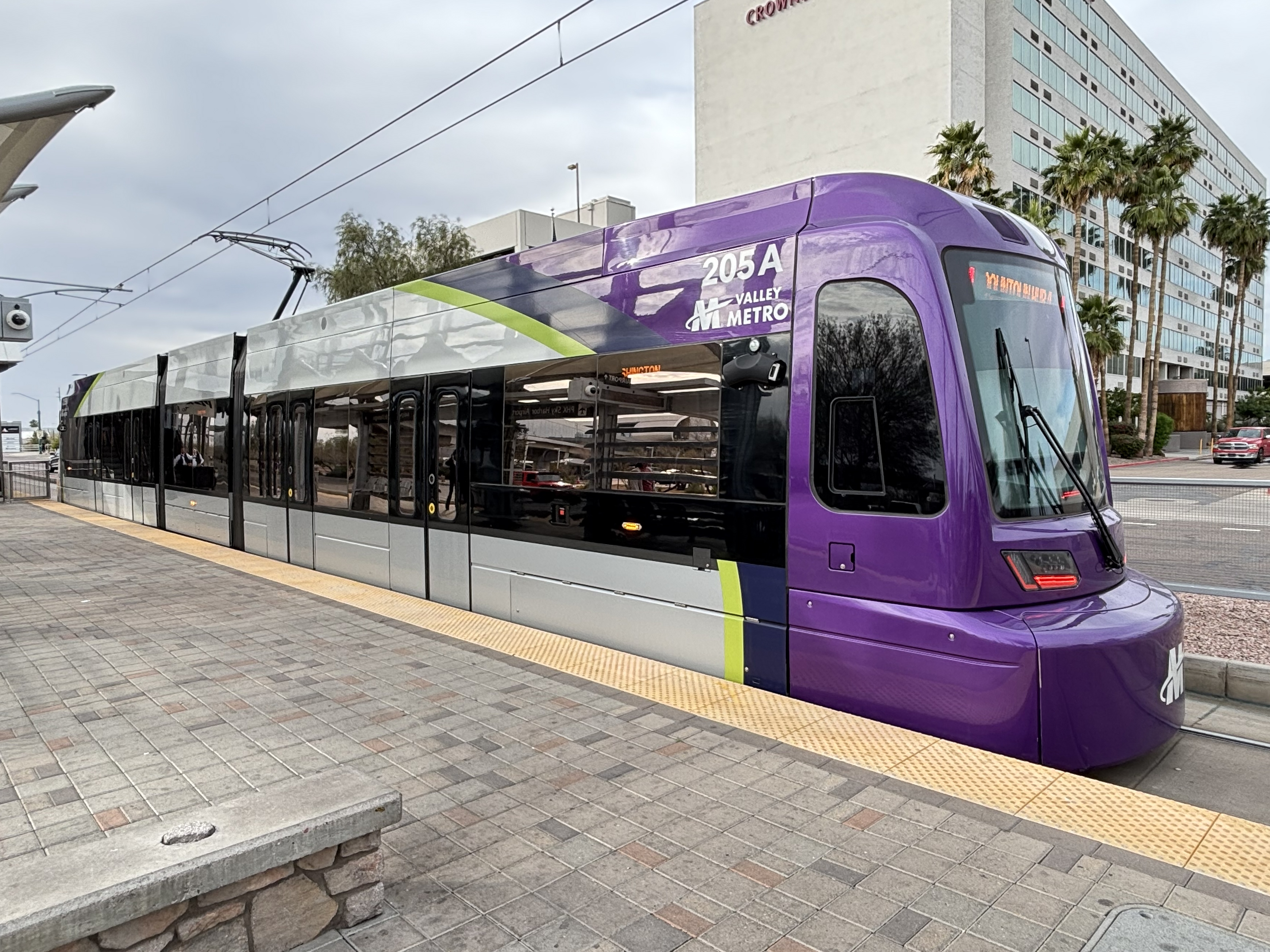 A gray and purple light rail train with a green stripe, number 205, traveling westbound on Washington Street in Phoenix