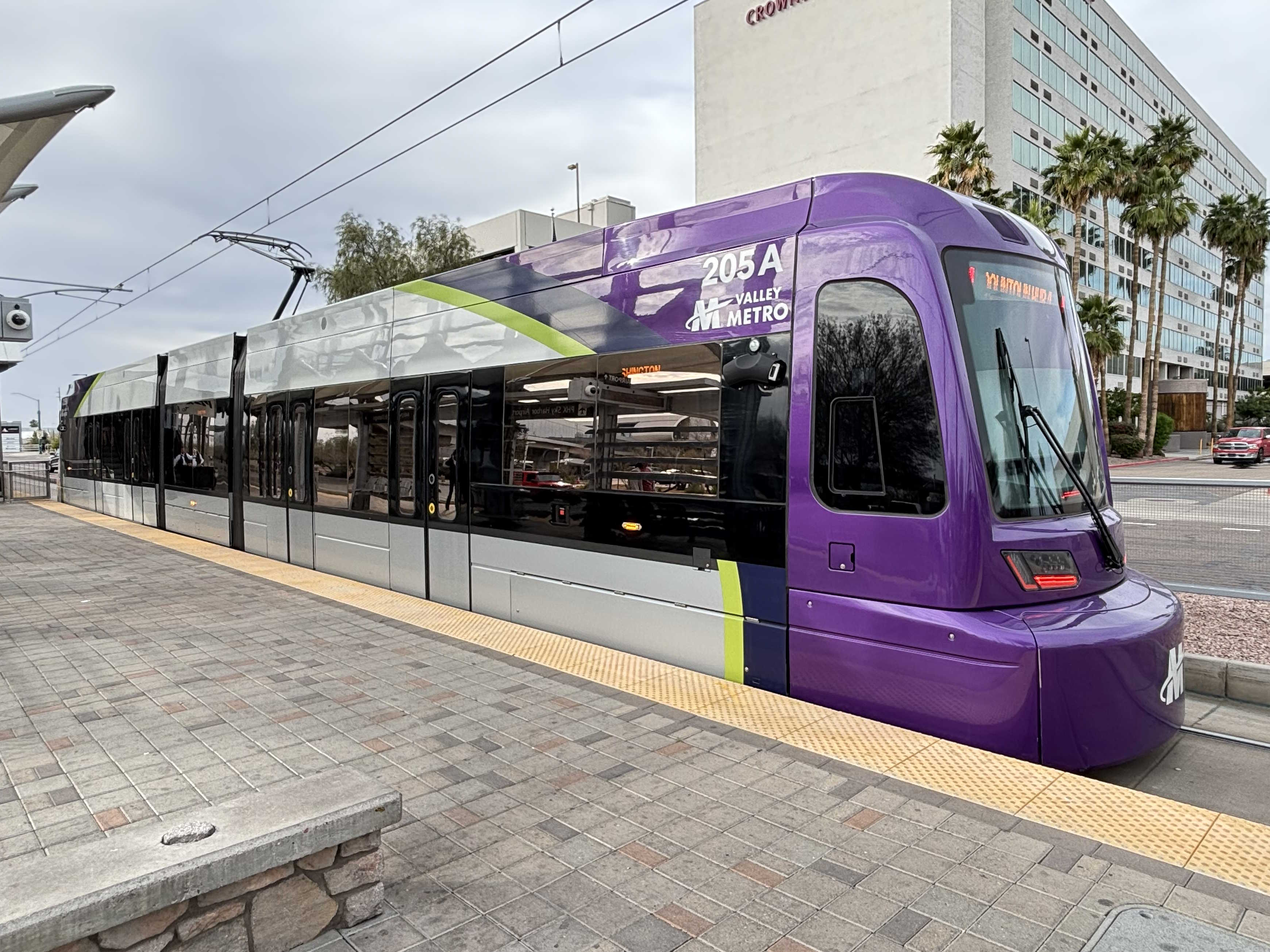 A gray and purple light rail train with a green stripe, number 205, traveling westbound on Washington Street in Phoenix
