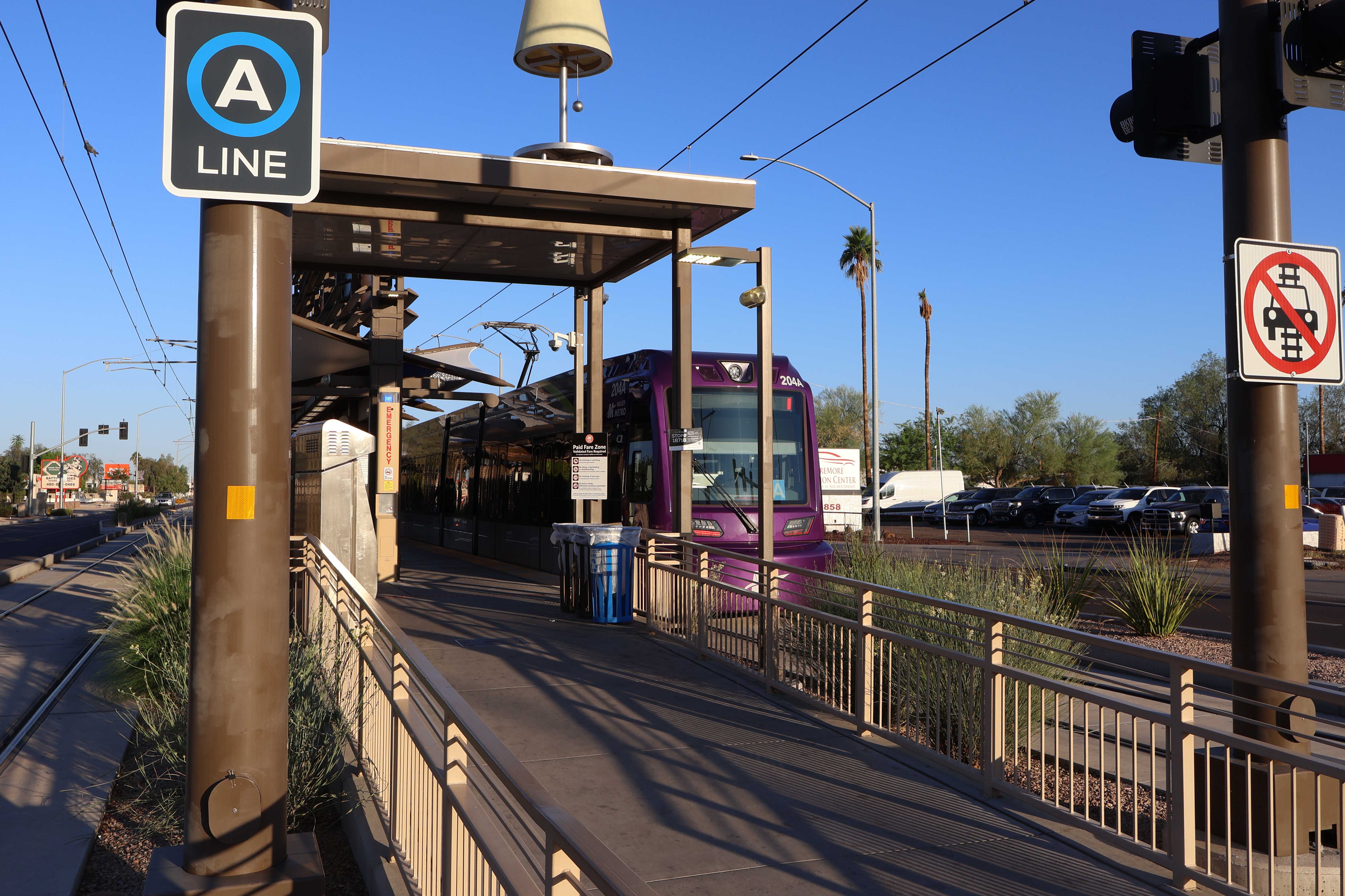 A gray and purple light rail train with a green stripe, number 204, parked at the Gilbert Road and Main Street station in Mesa