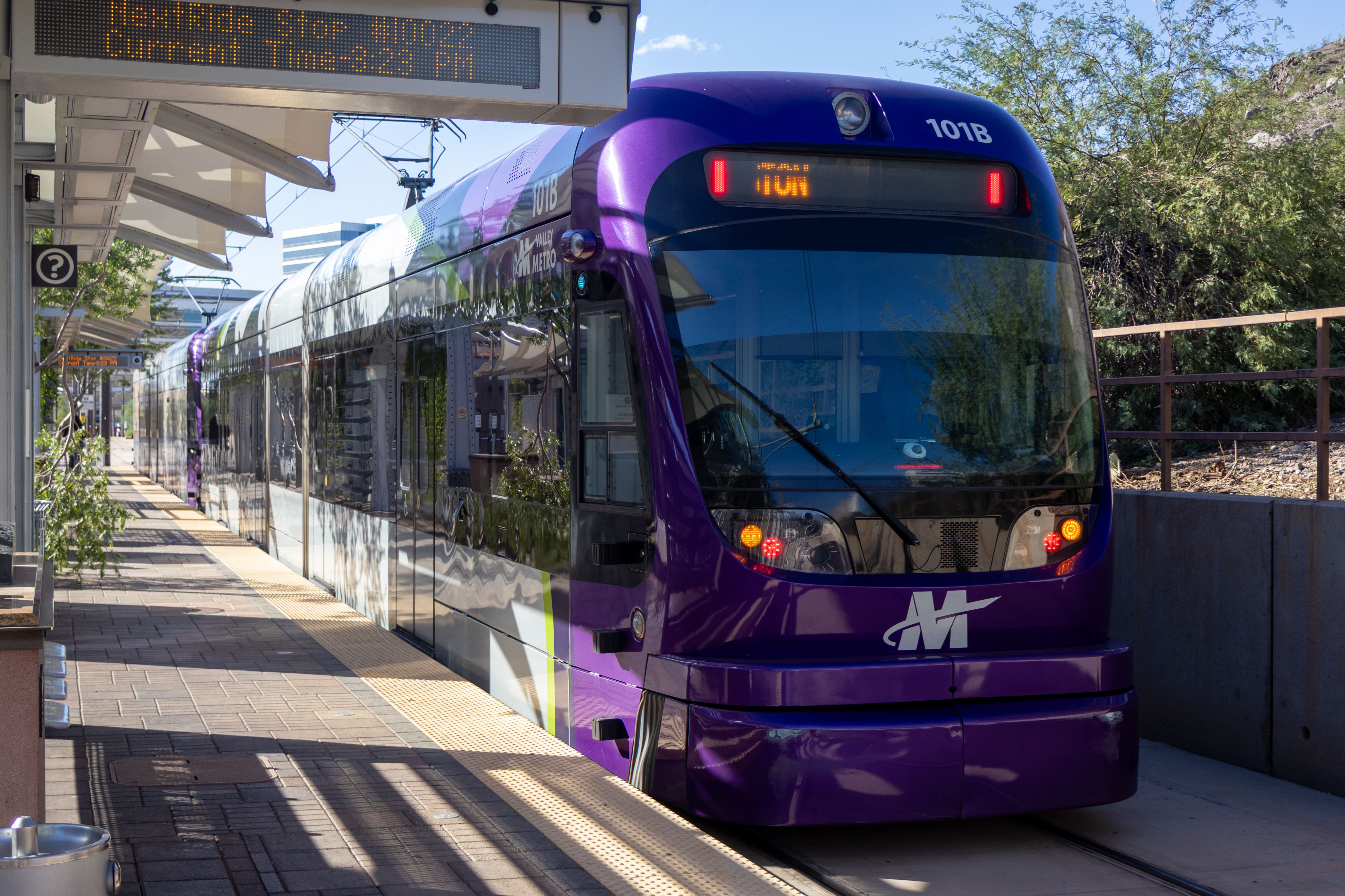A gray and purple light rail train with a green stripe, number 115, traveling eastbound on Jefferson Street in Phoenix