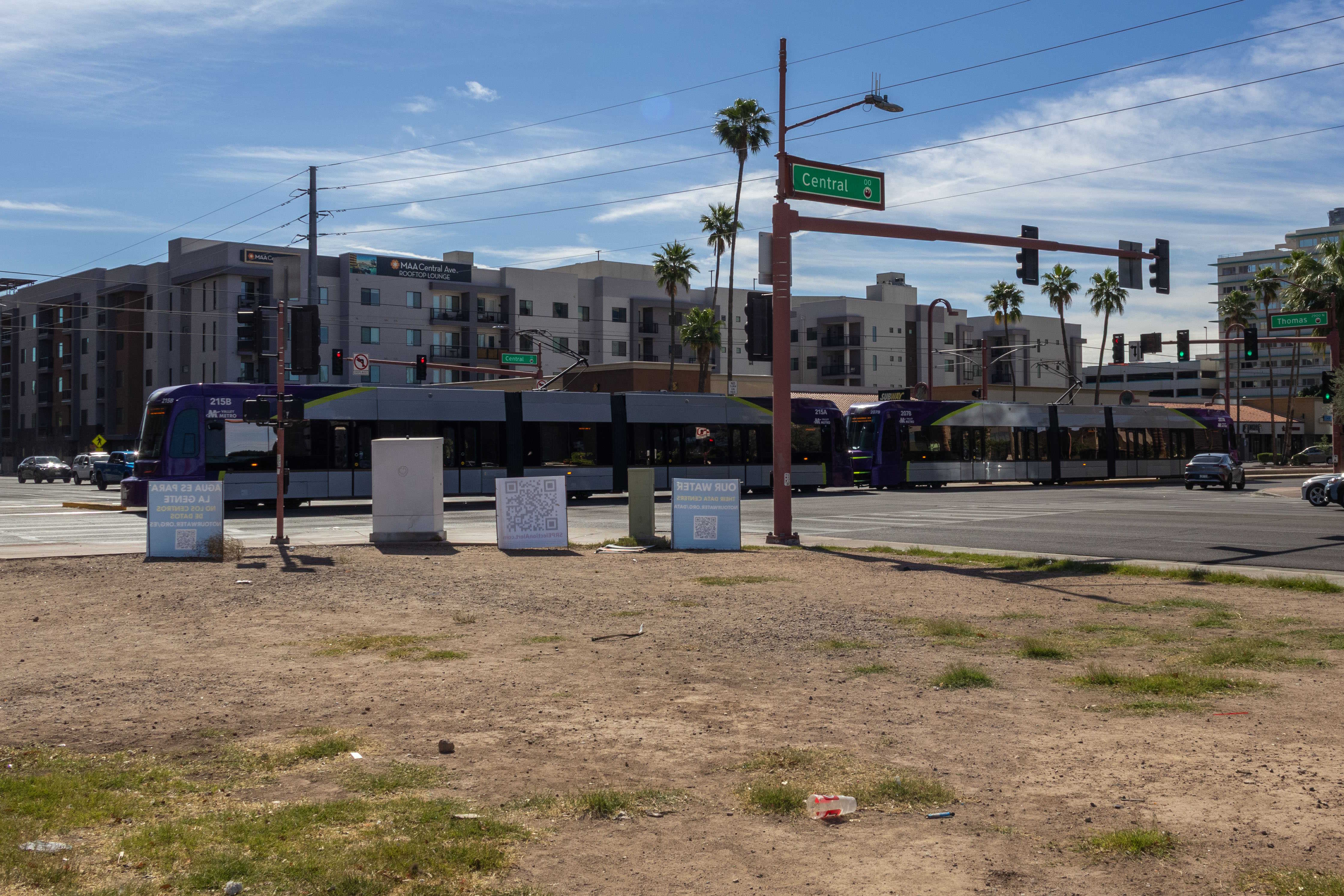 Two gray and purple light rail trains with green stripes, numbers 207 and 215, traveling southbound on Central Avenue in Phoenix