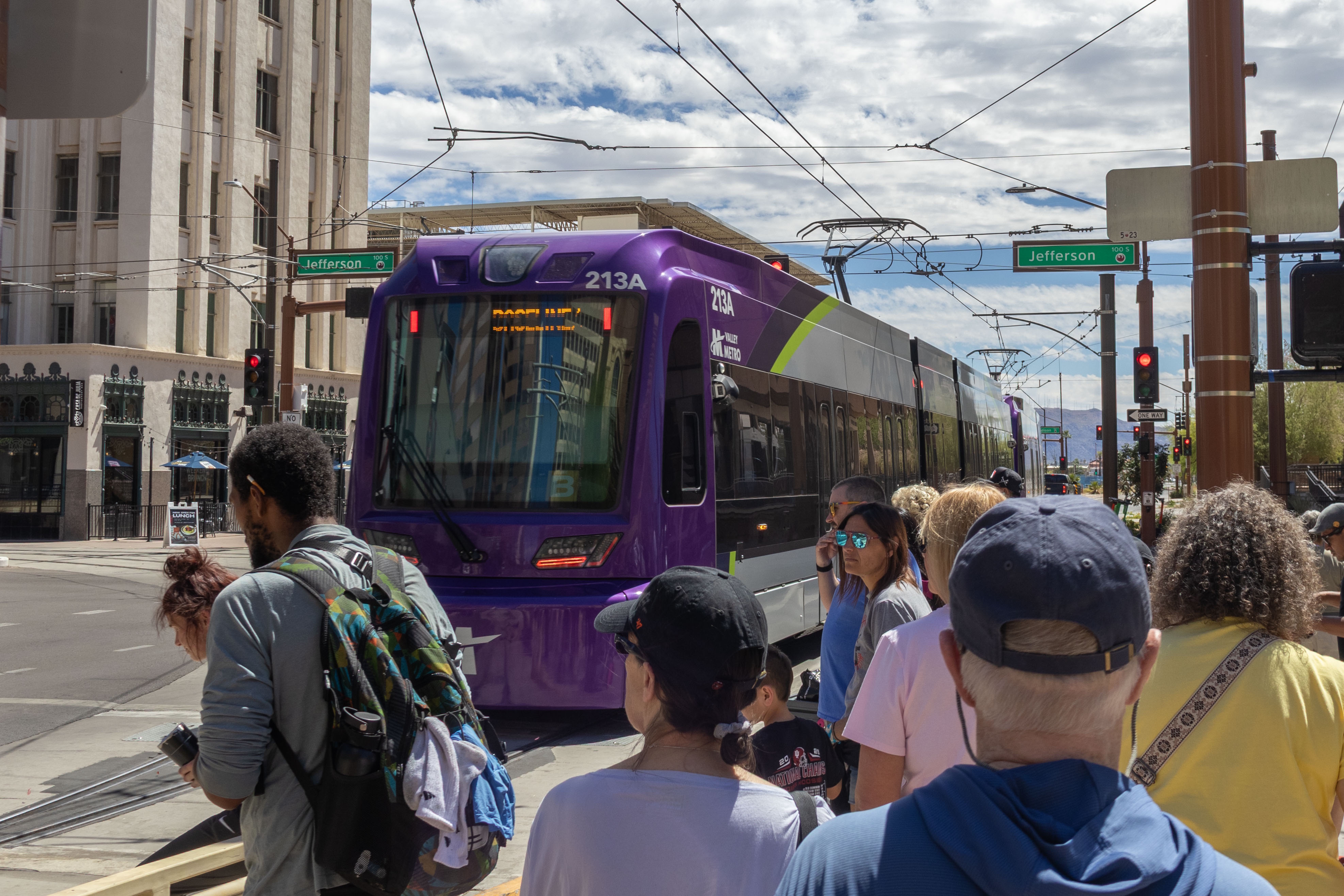 A gray and purple light rail train with a green stripe, number 213, traveling southbound on 1st Avenue in Phoenix