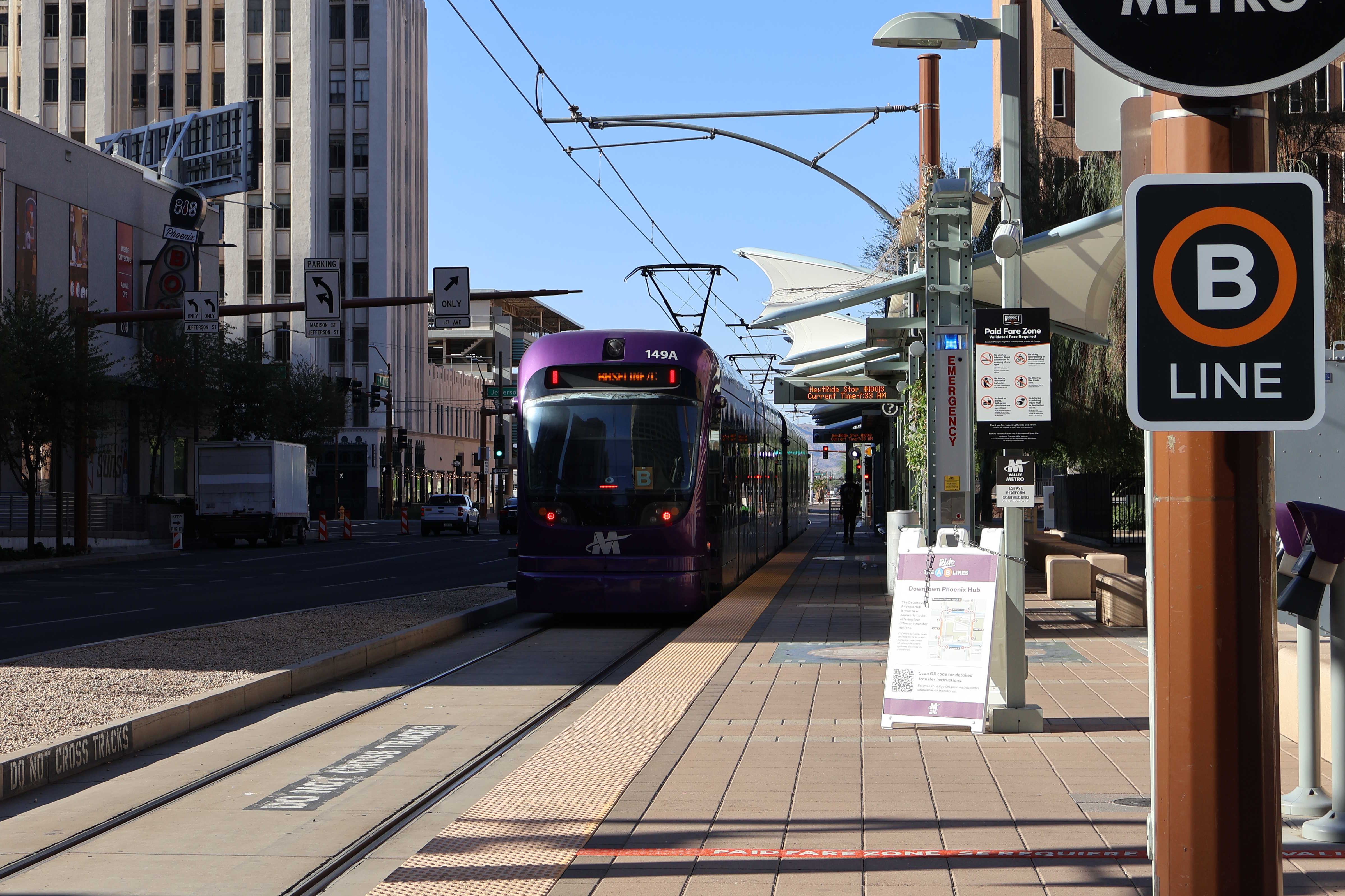 Two gray and purple light rail trains with green stripes, number 149 and another one unknown, traveling southbound on 1st Avenue in Phoenix