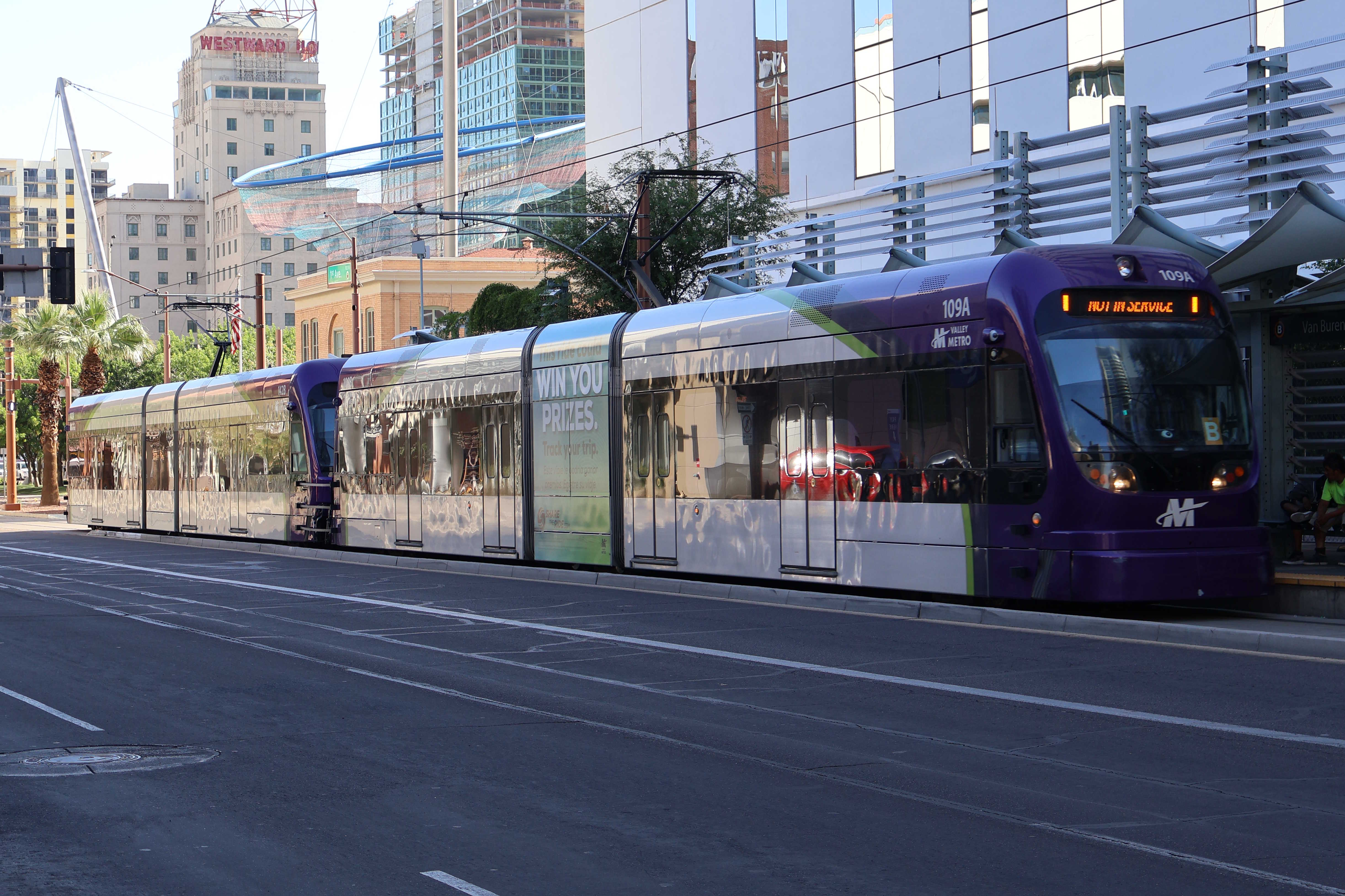 Two gray and purple light rail trains with green stripes, numbers 109 and 142, traveling southbound on 1st Avenue in Phoenix