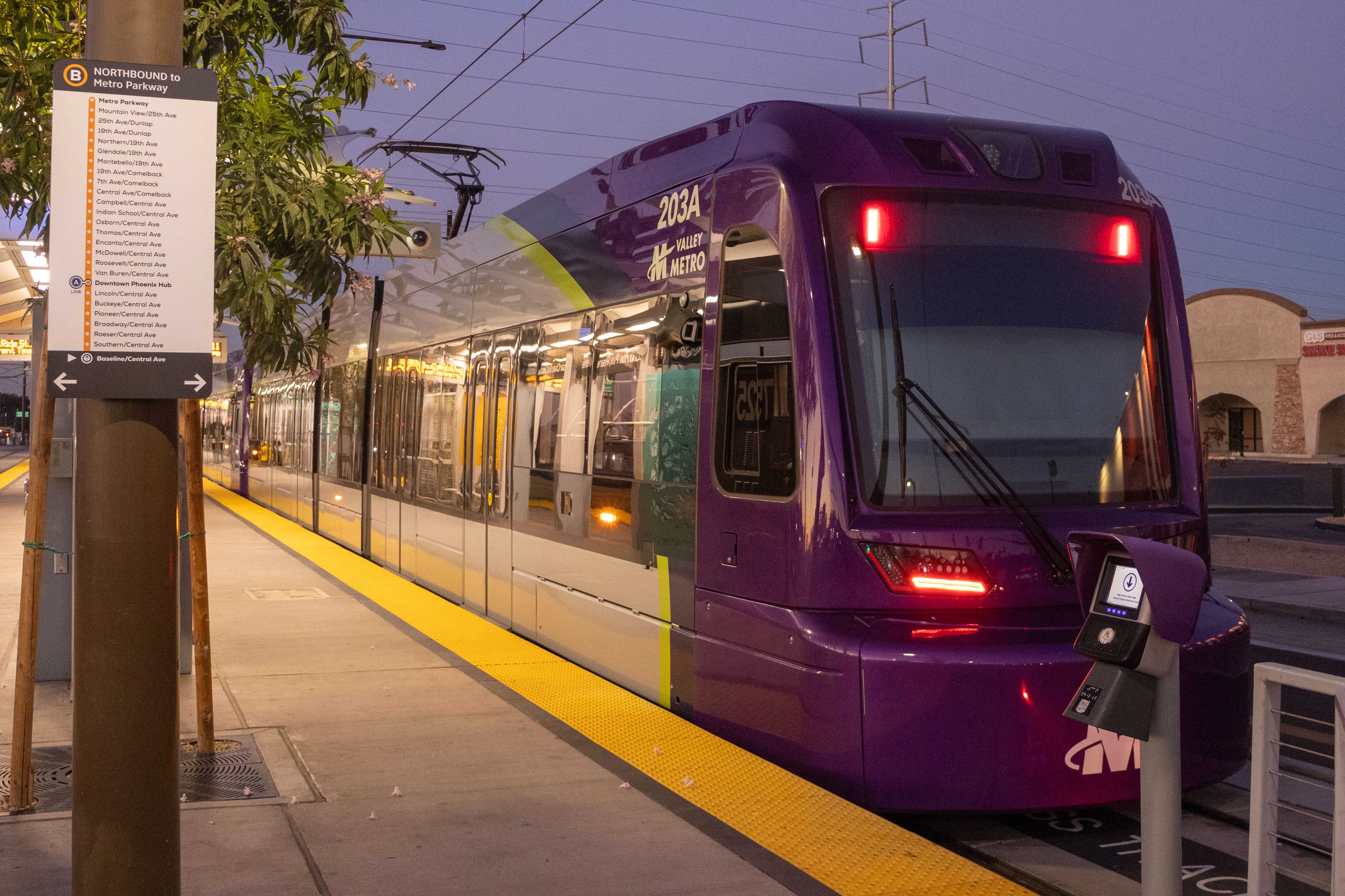 A gray and purple light rail train with a green stripe, number 203, traveling southbound on Central Avenue in Phoenix