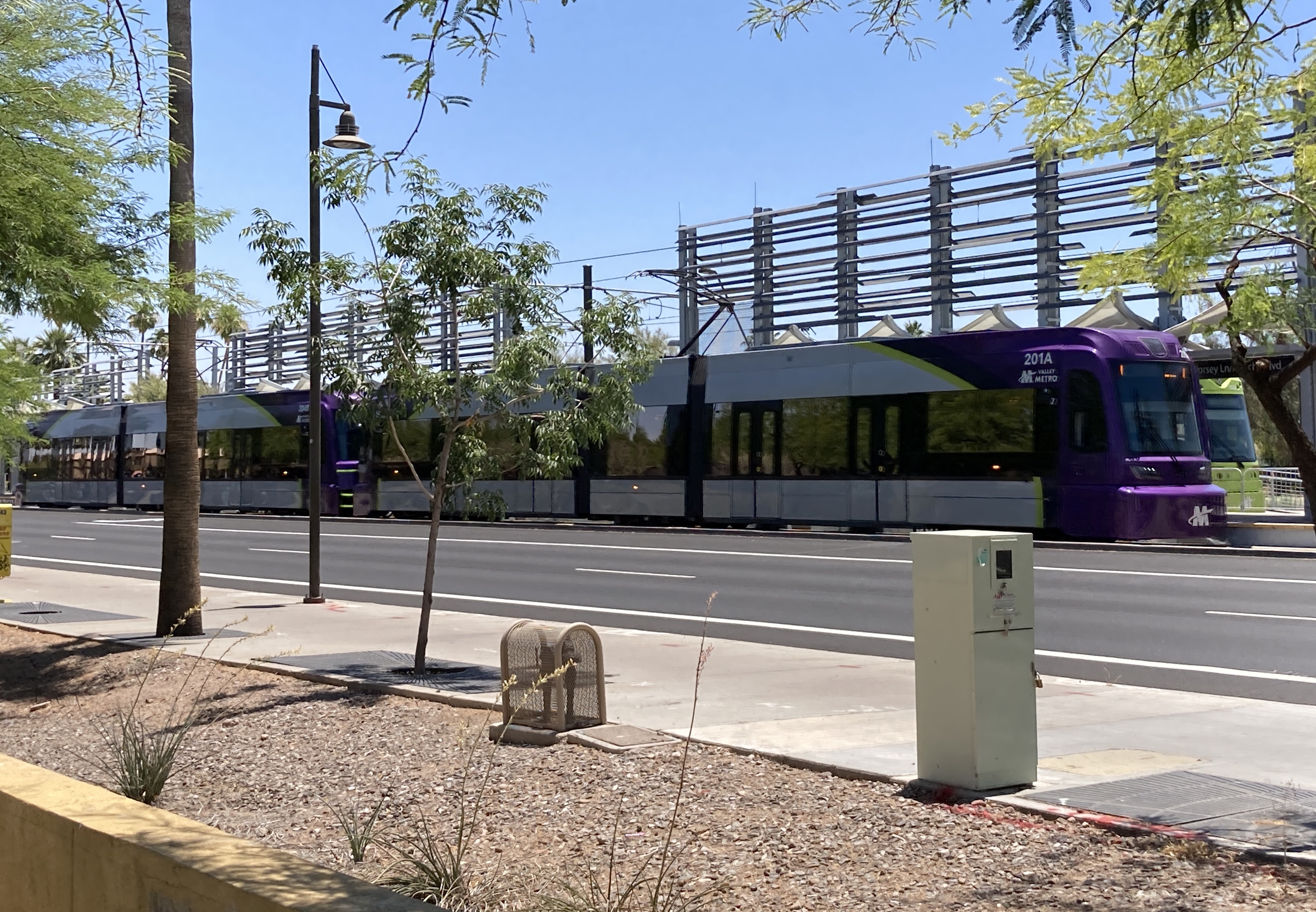 Two gray and purple light rail trains with green stripes, numbers 201 and 204, traveling westbound on Apache Boulevard in Tempe towards 19th Avenue and Dunlap station