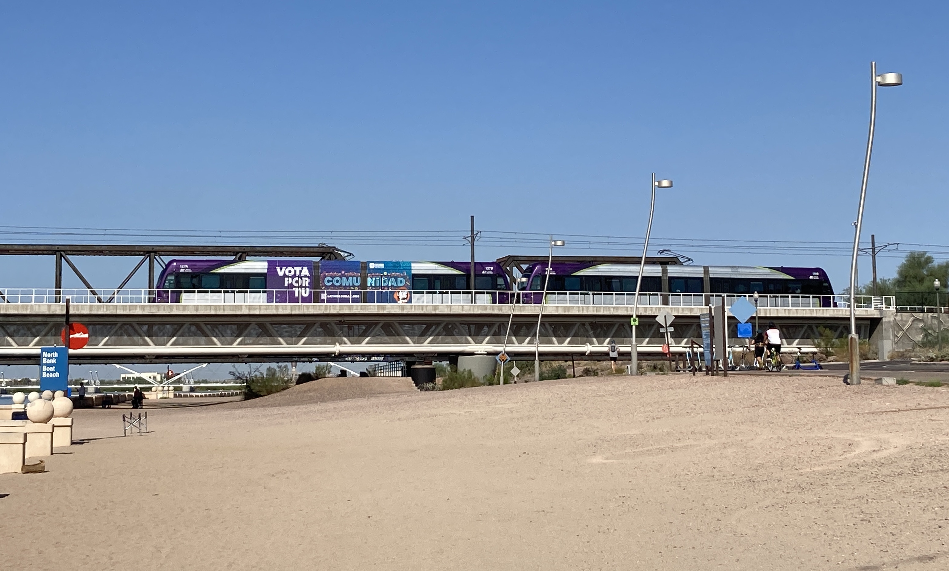 Two gray and purple light rail trains with green stripes, numbers 127 and 131, traveling eastbound over Tempe Town Lake towards Gilbert Road and Main Street station