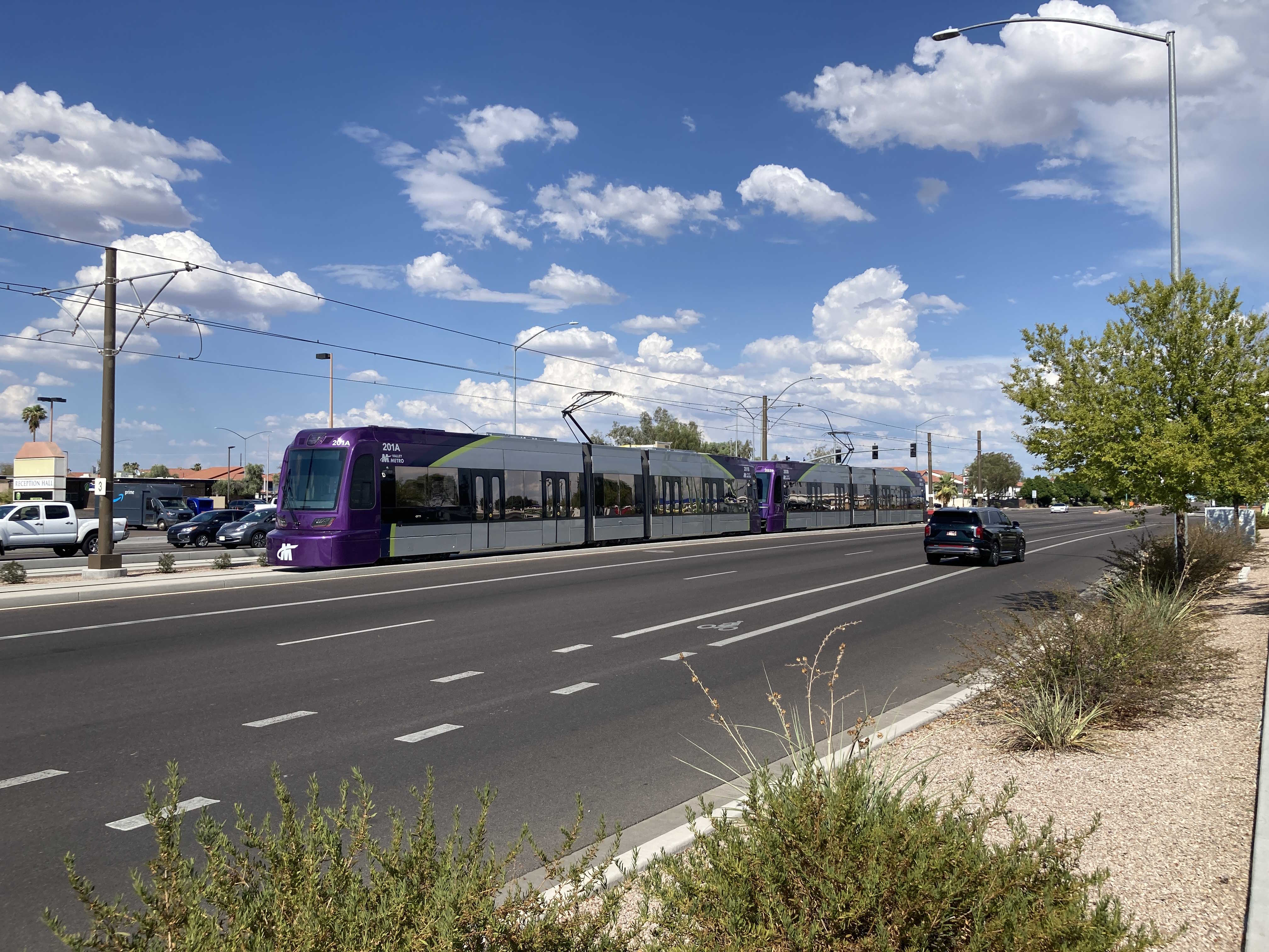 Two gray and purple light rail trains with green stripes, numbers 201 and 203, parked past the Gilbert Road and Main Street station