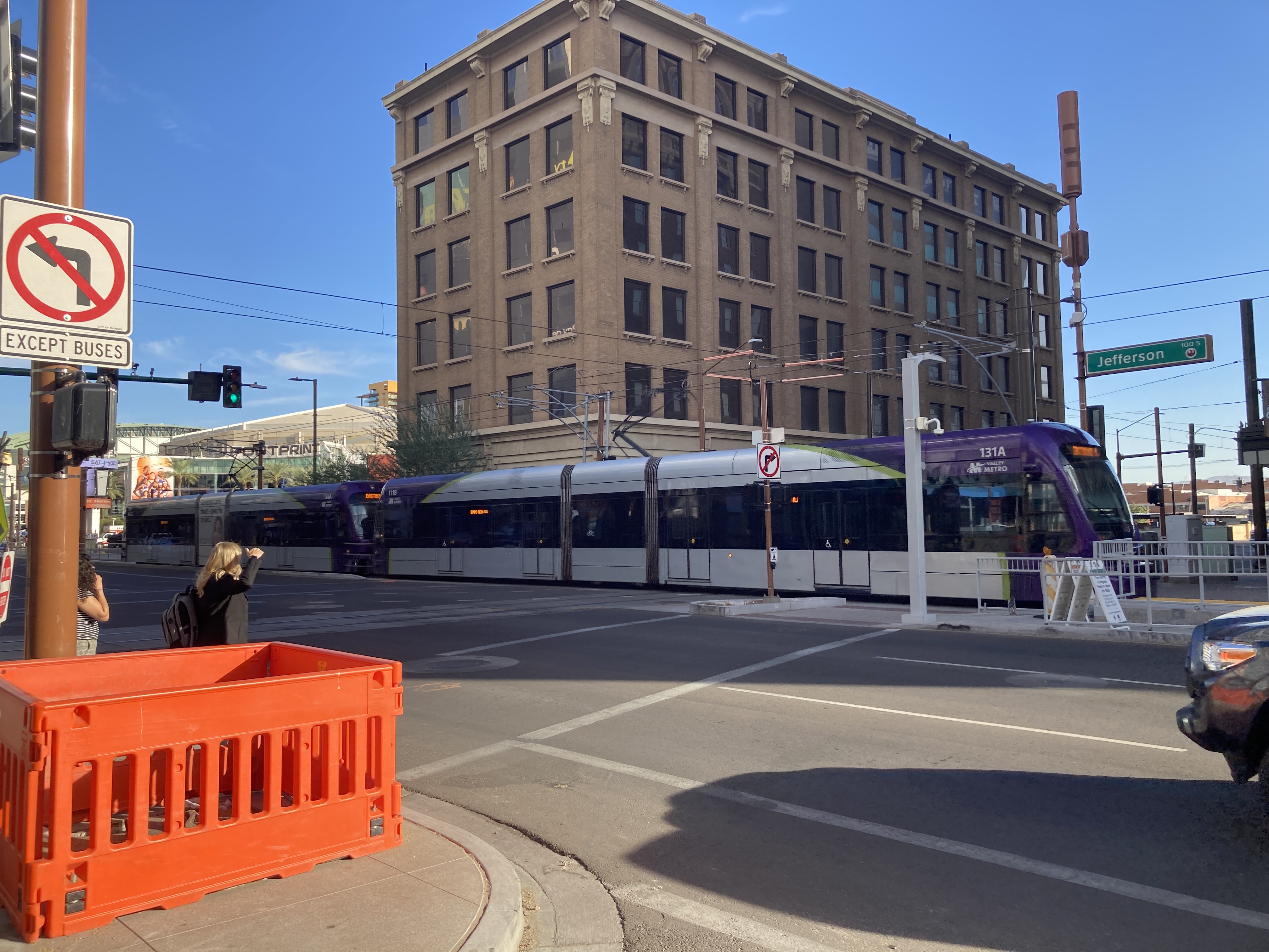 Two gray and purple light rail trains with green stripes, numbers 136 and 131, traveling eastbound on Jefferson Street in Phoenix towards Gilbert Road and Main Street station