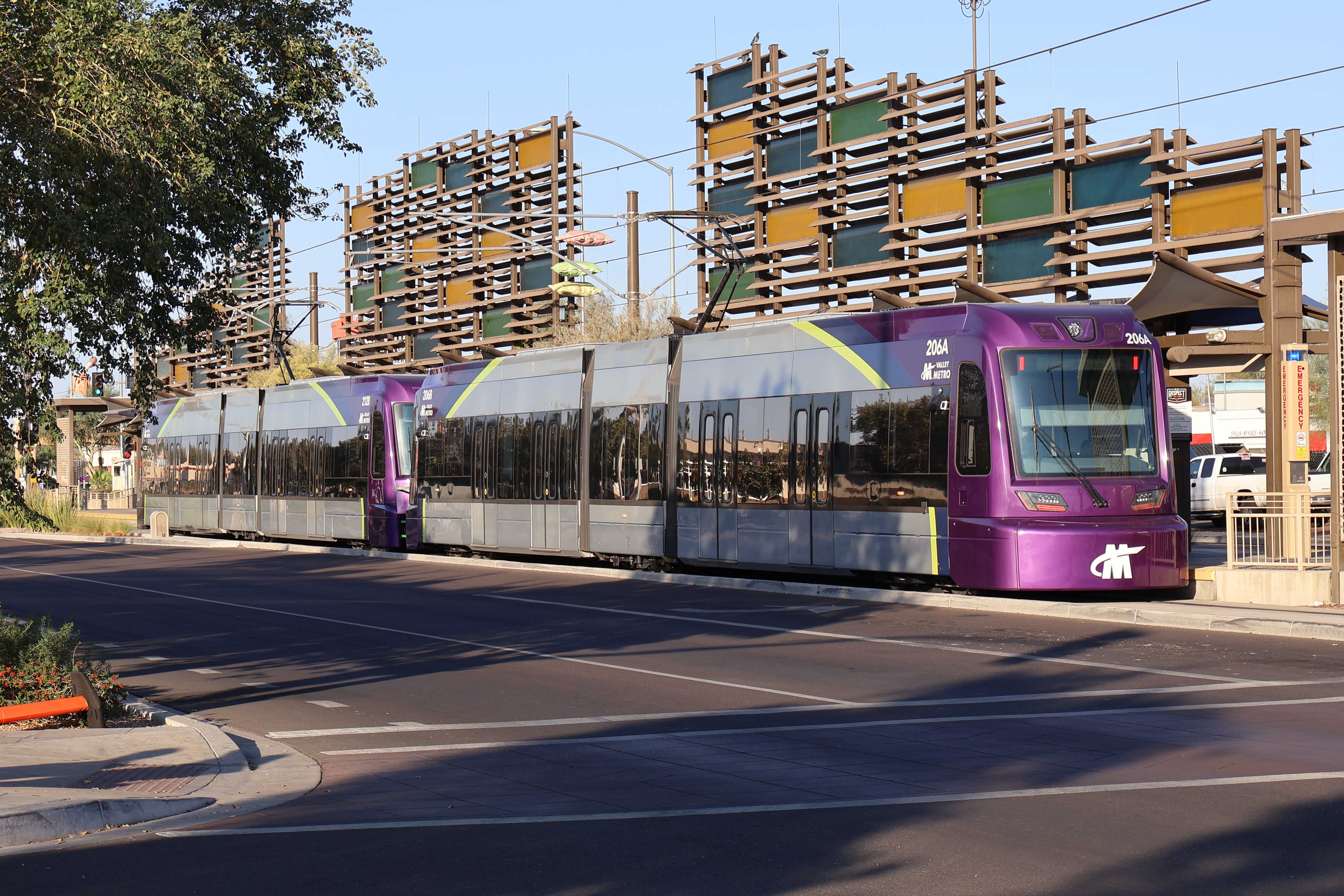 Two gray and purple light rail trains with green stripes, numbers 206 and 212, parked at the Gilbert Road and Main Street station