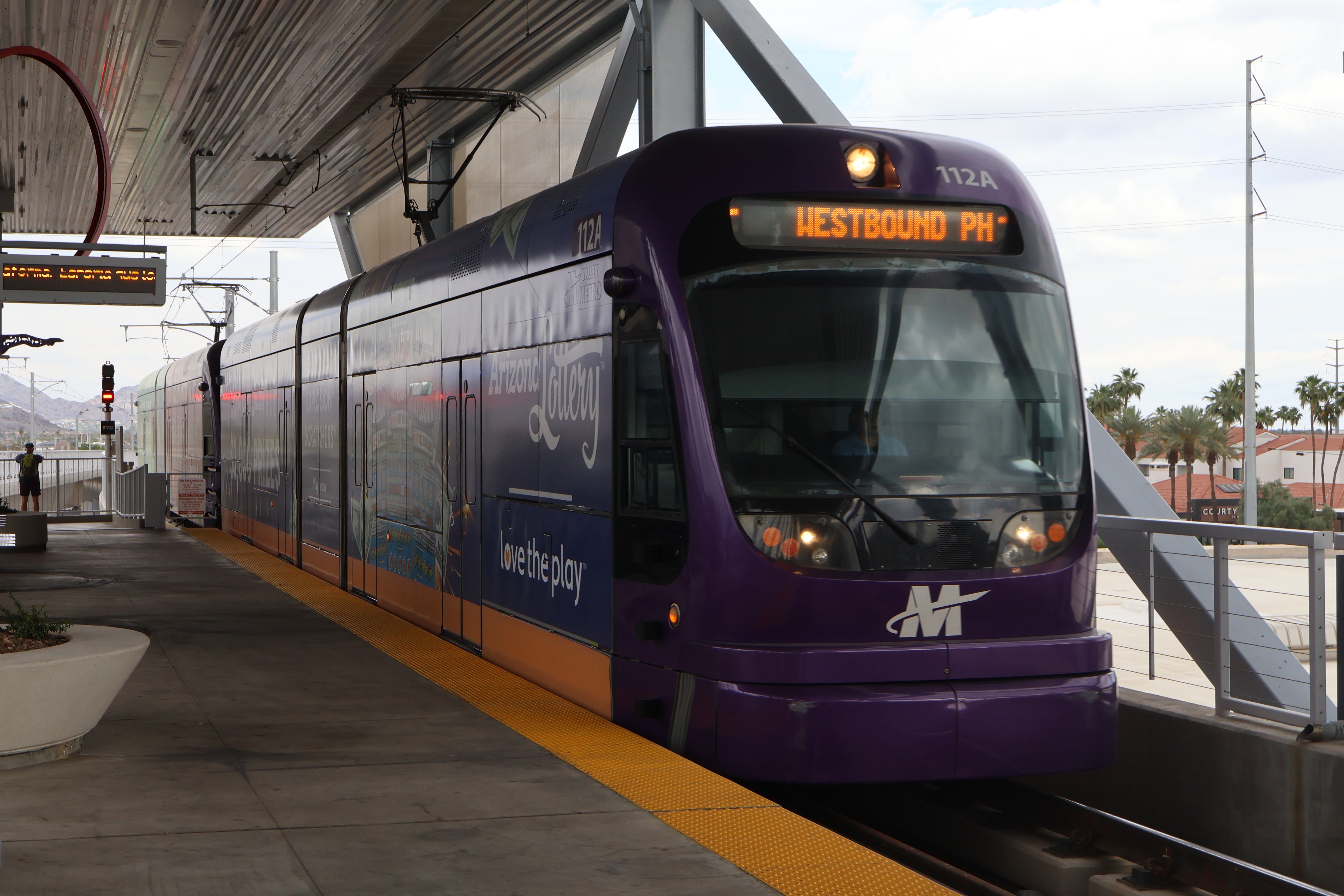 Two gray and purple light rail trains with green stripes, number 112 and another one unknown, at Metro Parkway Phoenix