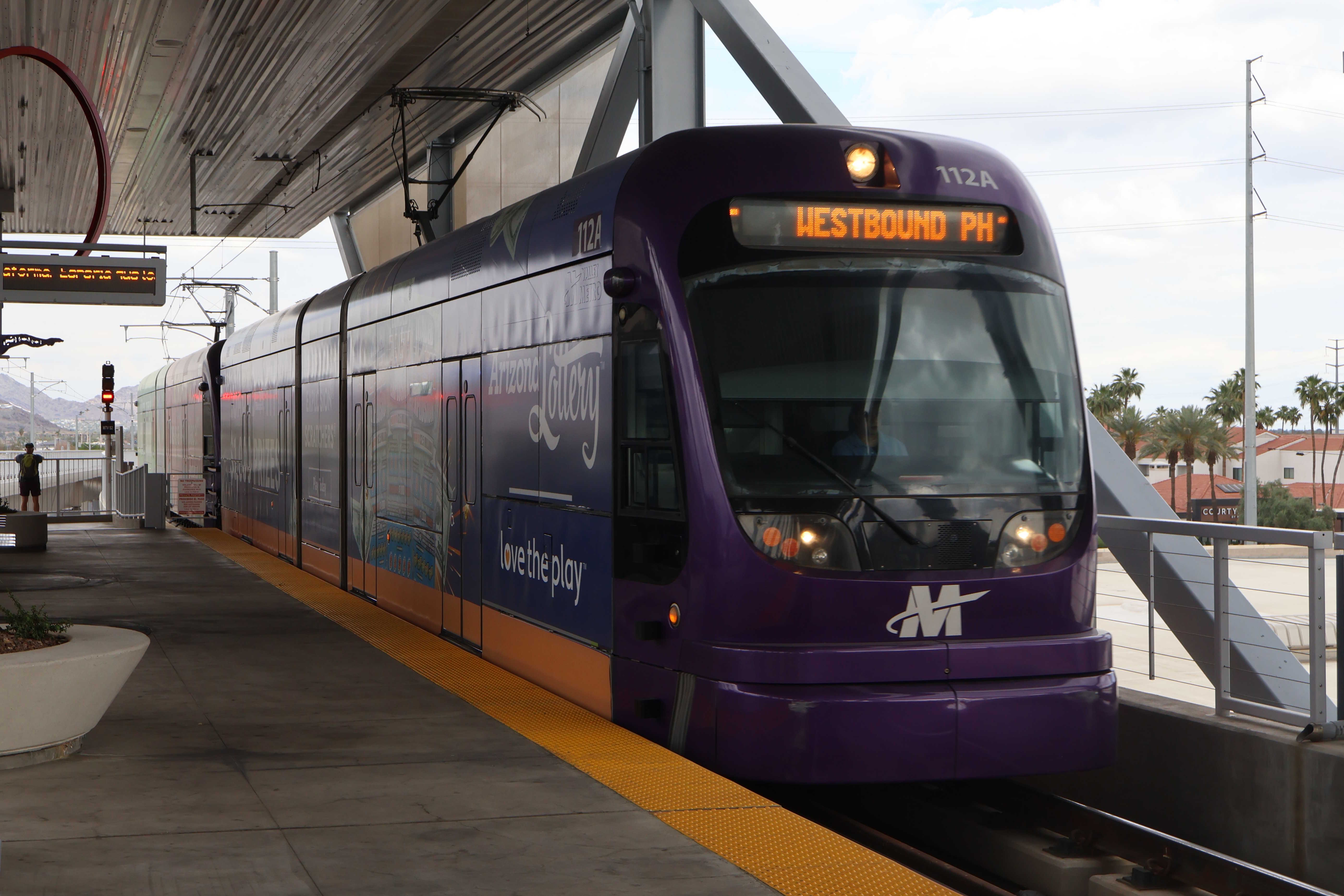 Two gray and purple light rail trains with green stripes, number 112 and another one unknown, at Metro Parkway Phoenix