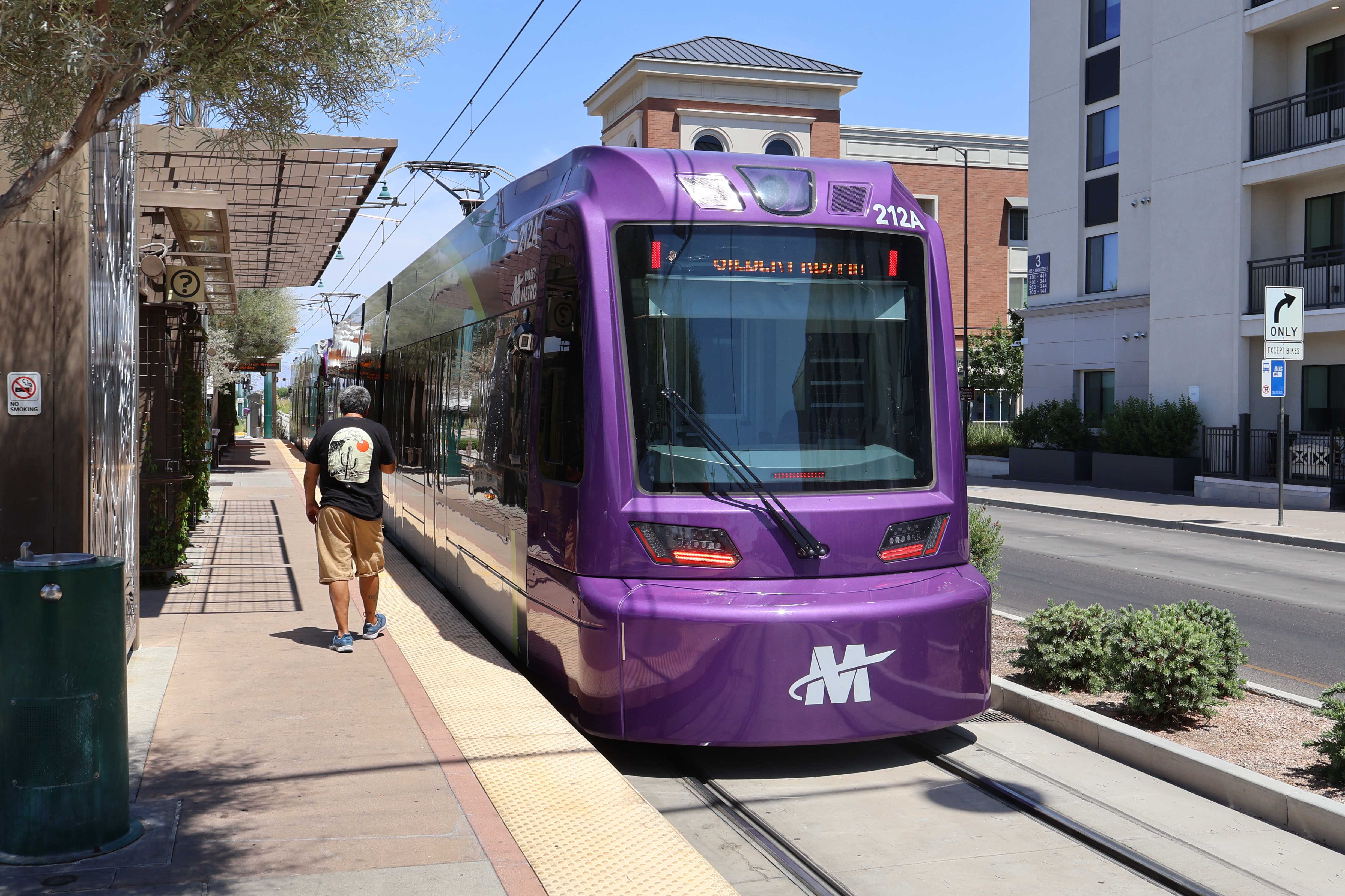 A gray and purple light rail train with a green stripe, number 212, traveling eastbound on Main Street in Mesa