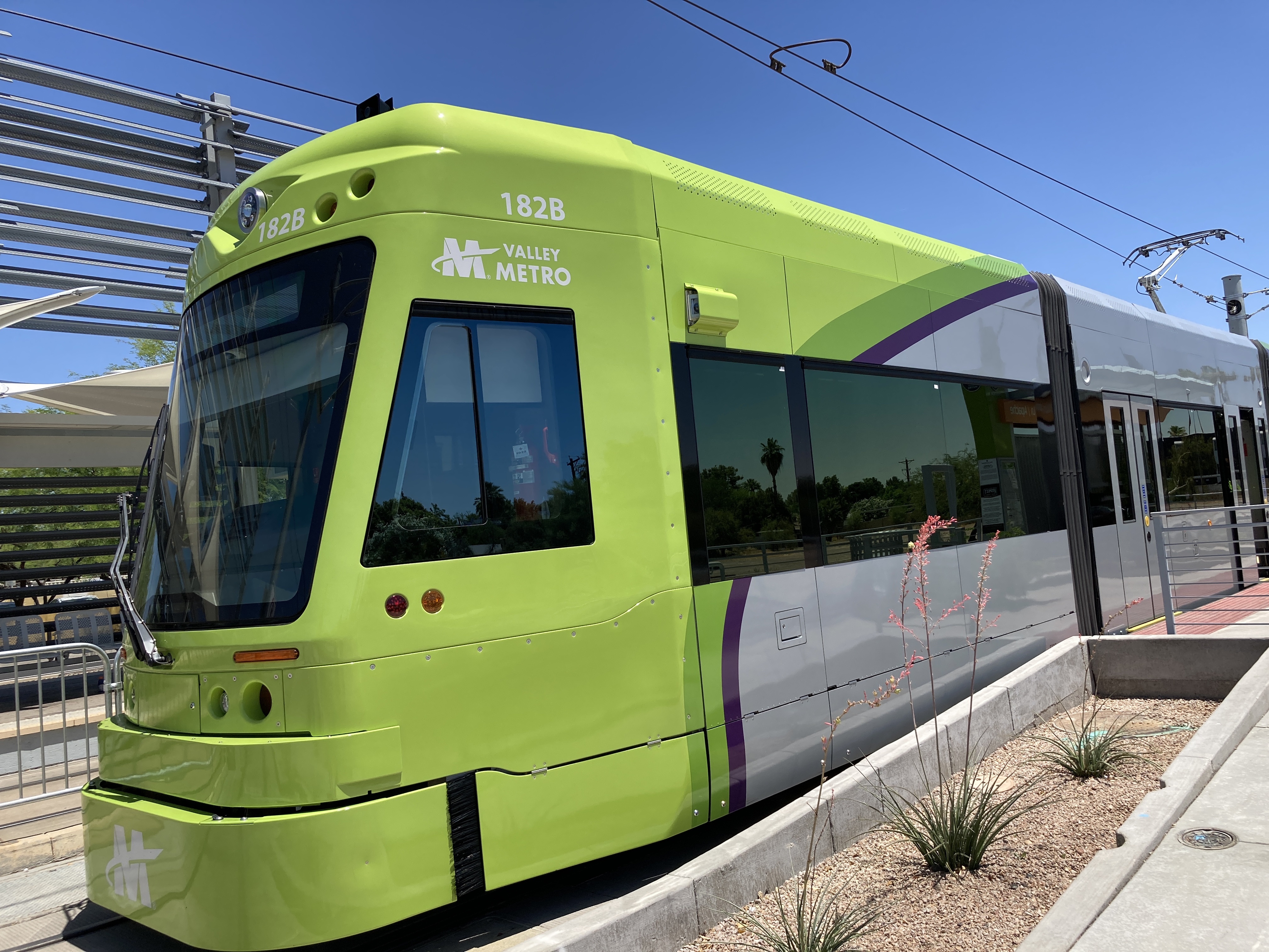 A bright green and gray streetcar with a darker green and purple stripe, number 182, at Dorsey and Apache station