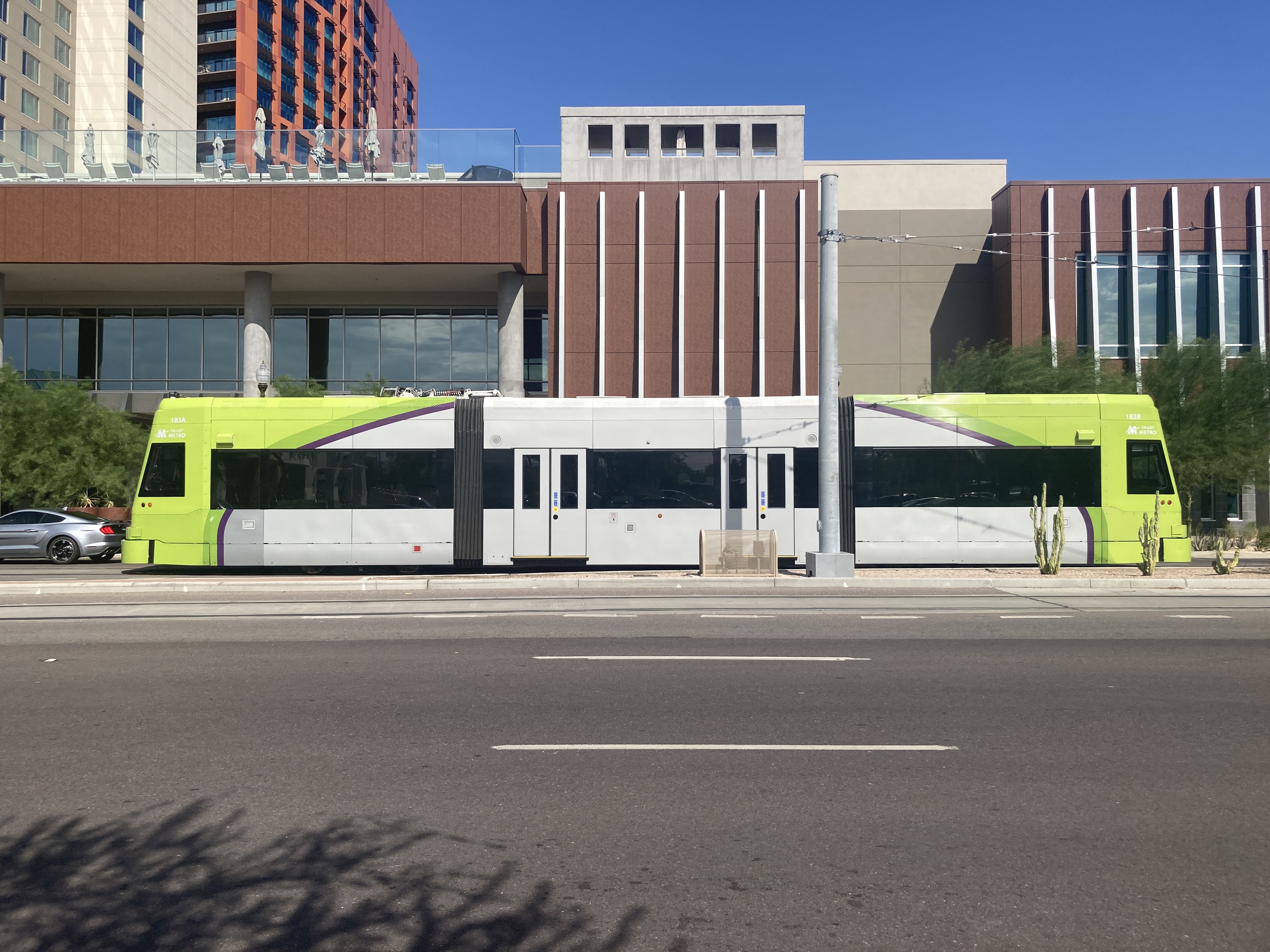 A bright green and gray streetcar with a darker green and purple stripe, number 183, at Mill Avenue and University Drive