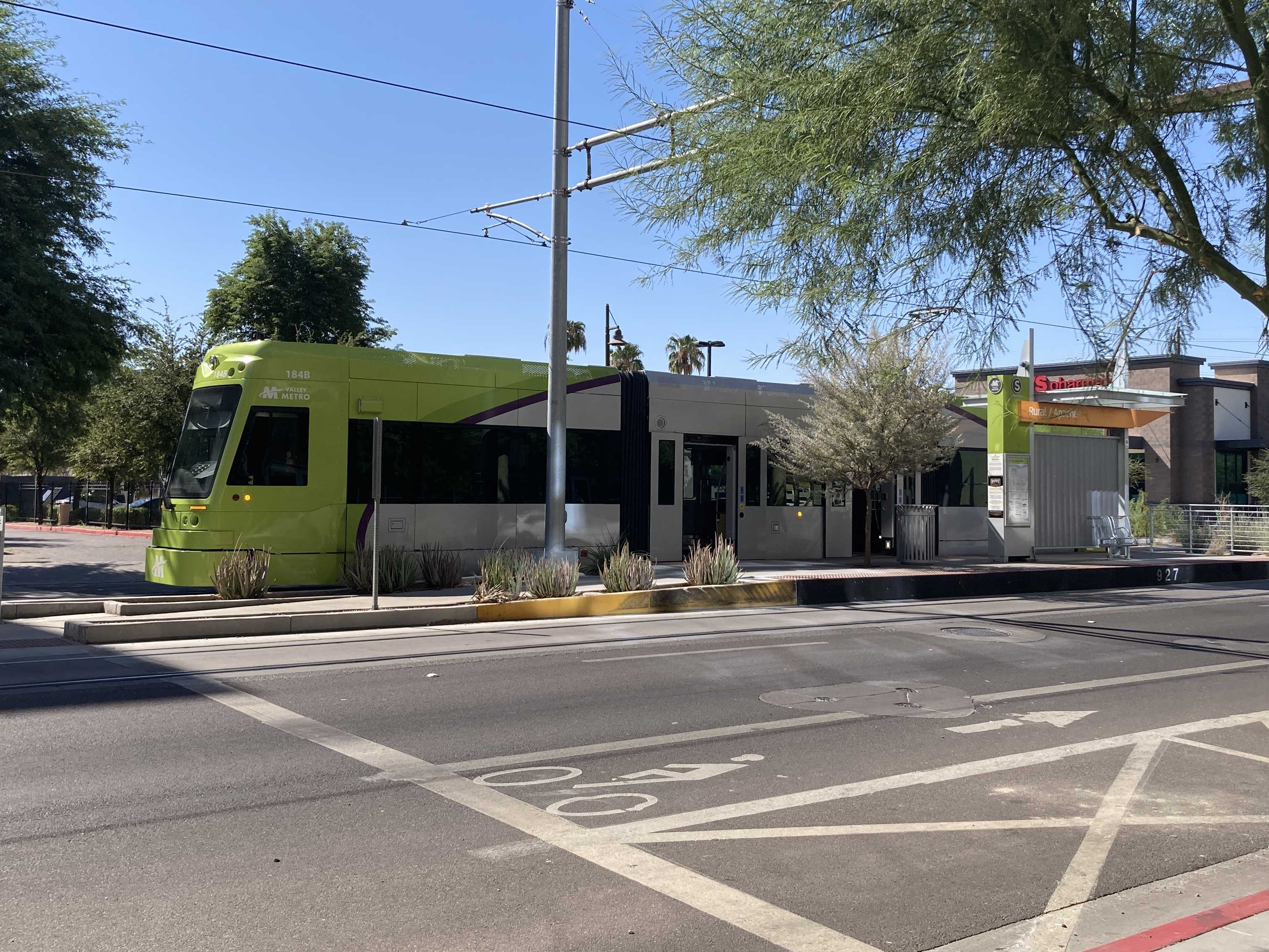 A bright green and gray streetcar with a darker green and purple stripe, number 184, at Rural and Apache station